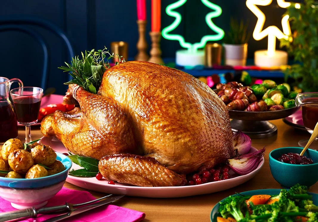 A roasted turkey on a platter surrounded by vegetables, cranberry sauce, and festive decorations.