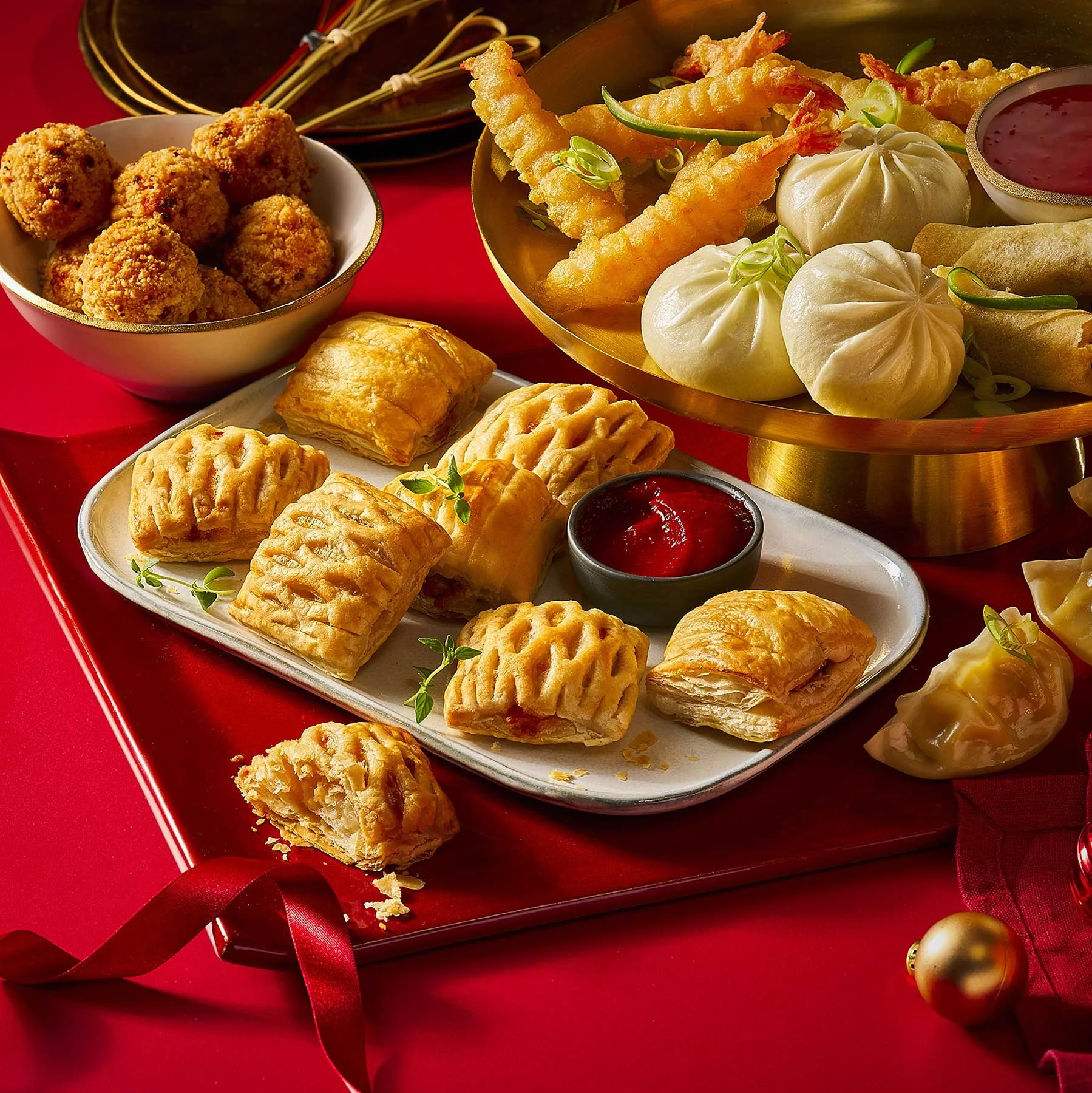 A variety of Chinese dim sum dishes including potstickers, fried shrimp, fried meatballs, and golden pastries served on a red table with red ribbon and holiday decorations.