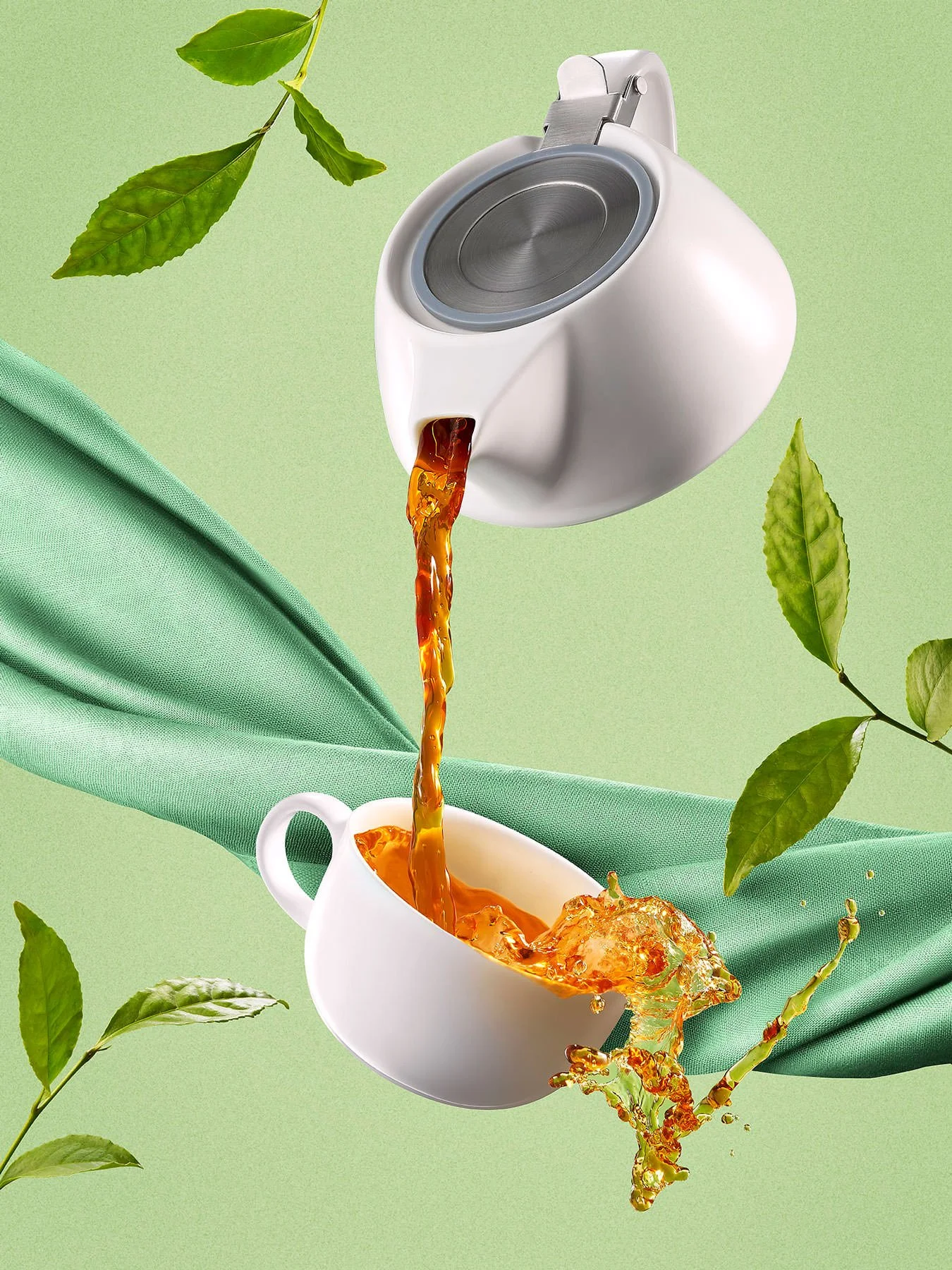 A white teacup being filled with tea from a modern white teapot, surrounded by green leaves and a draped green cloth, set against a light green background.