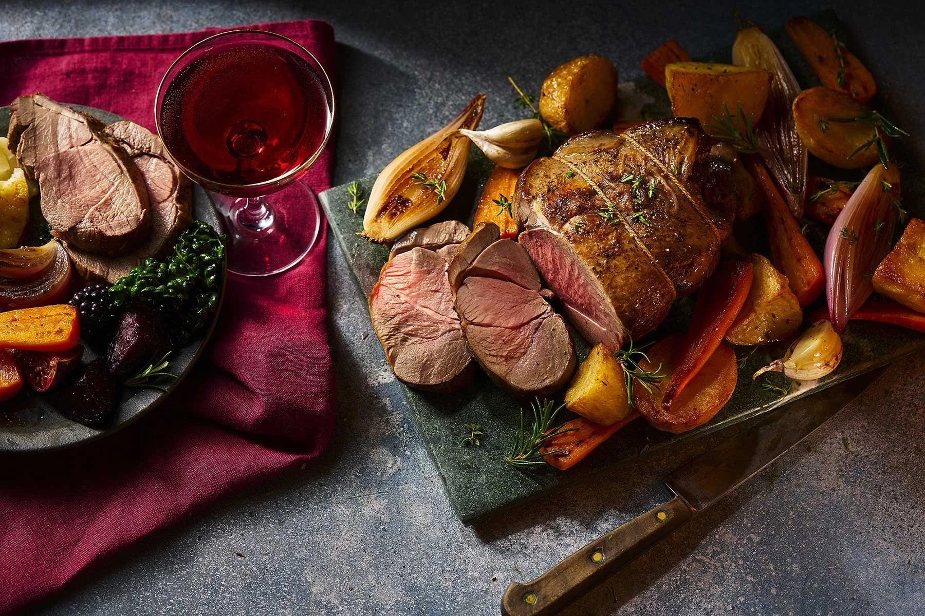 A cooked meat roast with vegetables and a glass of red wine on a table.
