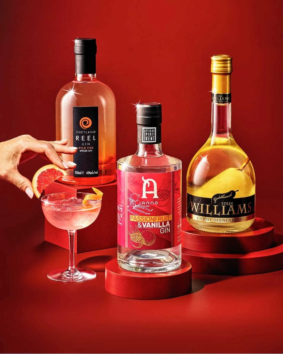 Three bottles of alcoholic beverages on red platforms with a hand placing a grapefruit wedge into a cocktail glass.