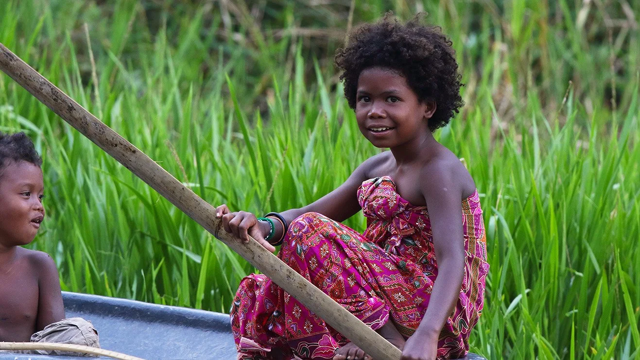 Orang Asli siblings sitting quietly in a small boat on a river, Malaysia