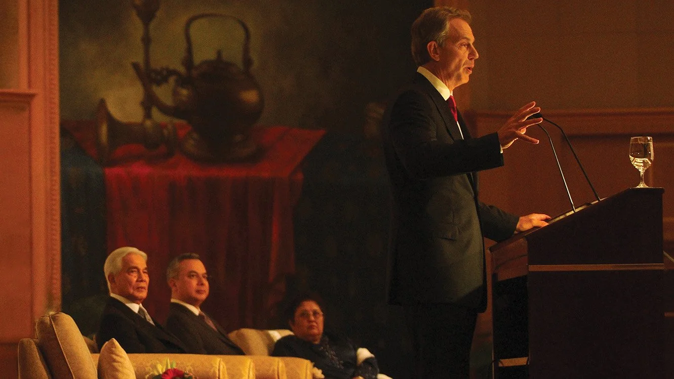 Tony Blair delivering a public speech, captured side profile under stage lighting