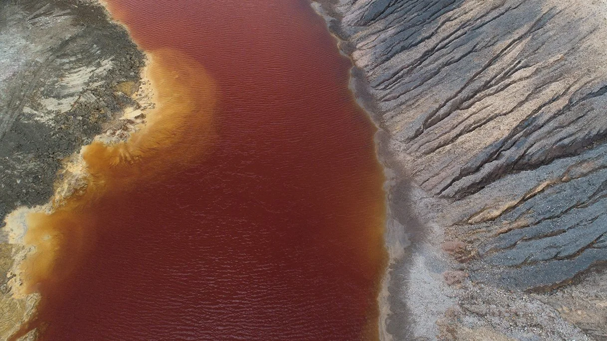 Aerial photograph of a tin mine in Pengkalan Hulu, Malaysia, with copper-coloured water and patterned sand banks forming painterly abstract shapes.