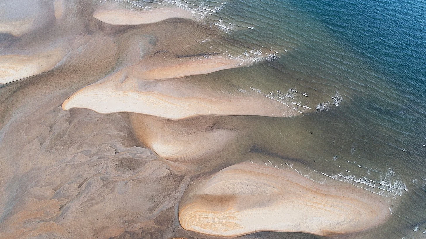 Aerial view of beachscapes with abstract sandbars and shallow water patterns shaped by tide and current.