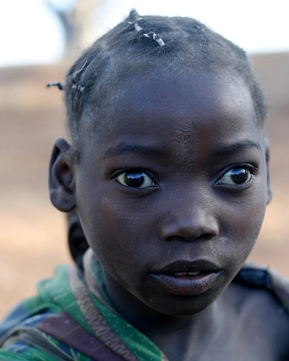 Young girl photographed in Mozambique, standing still and looking directly at the camera.