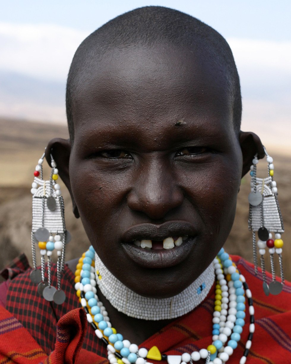 Maasai girl photographed in traditional attire, standing calmly and meeting the camera’s gaze.
