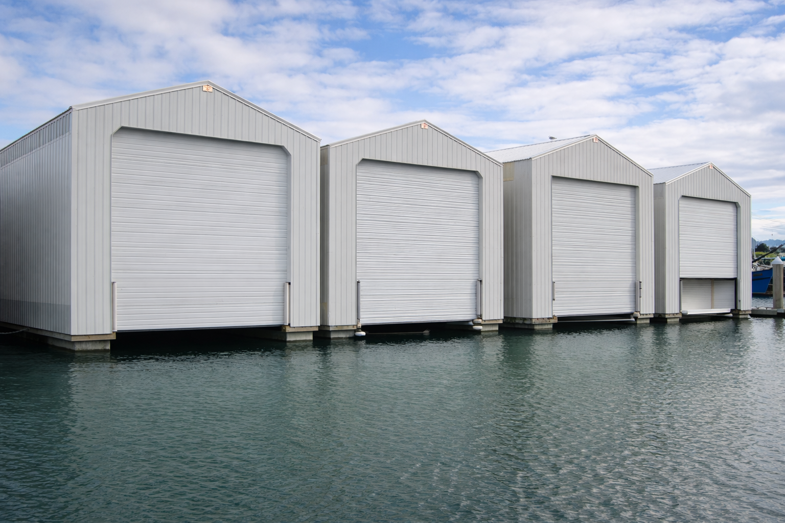 Four white boat storage garages on a dock over water with cloudy sky in the background.
