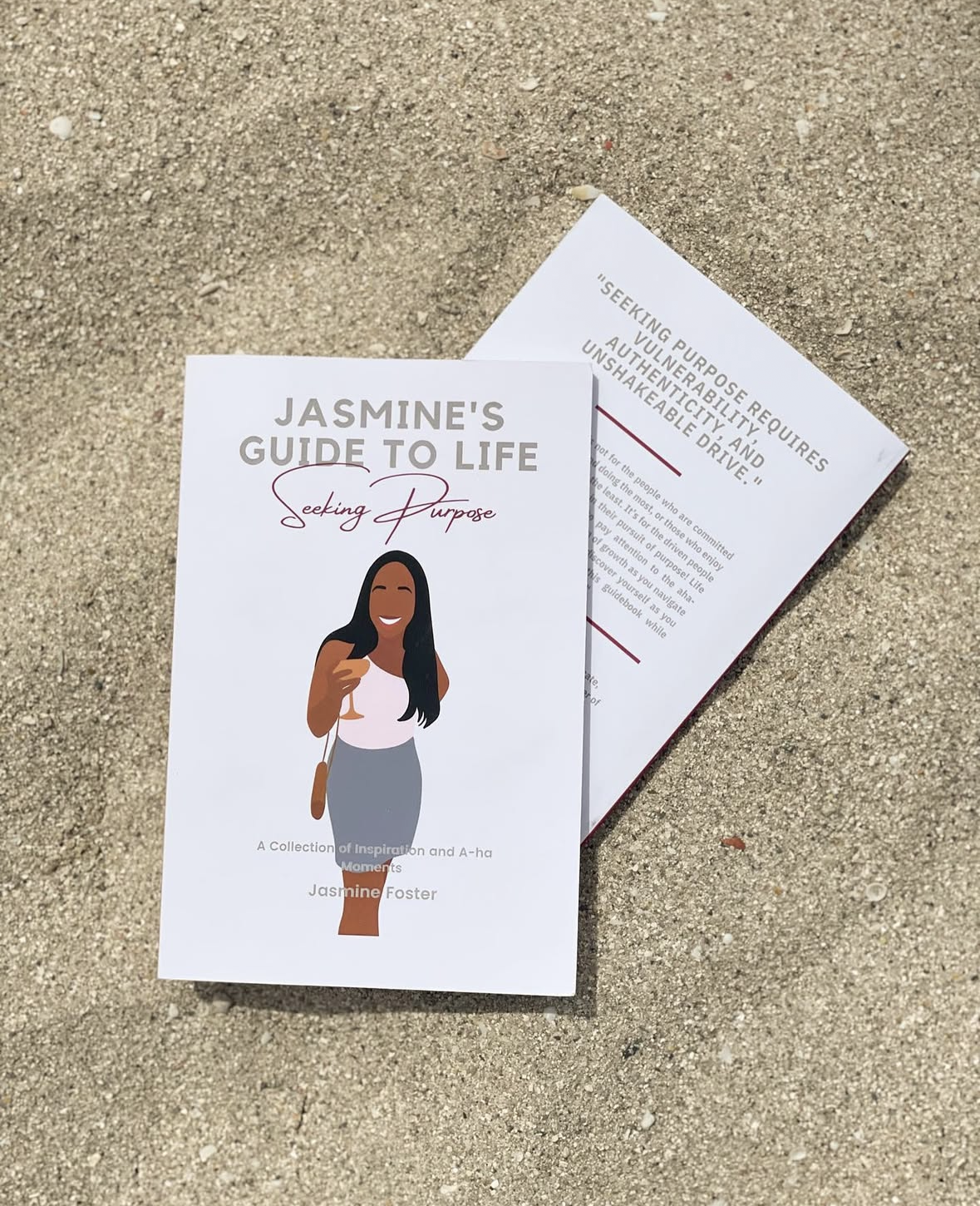 A magazine titled "Jasmine's Guide to Life: Seeking Purpose" lying on sandy ground, featuring an illustration of a woman with long black hair holding a glass of champagne.