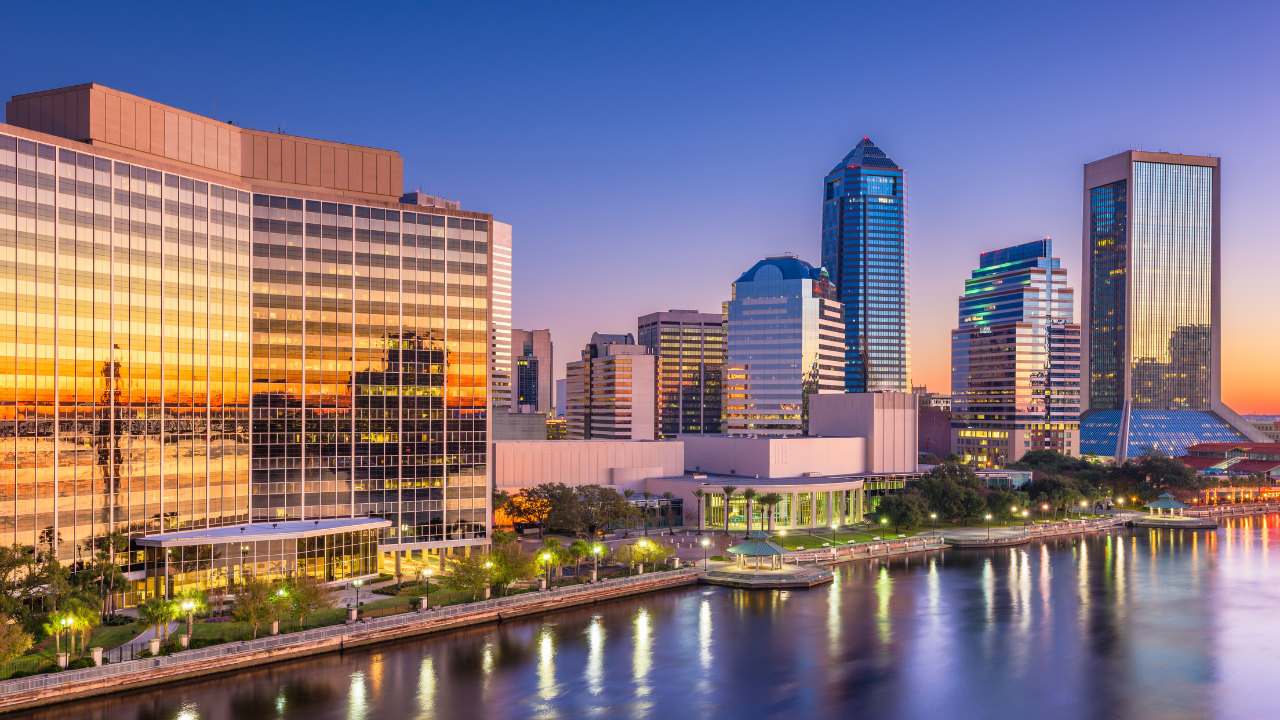 City skyline at sunset with tall buildings reflecting on the water.