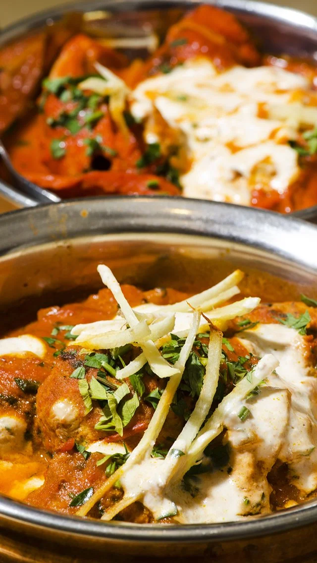 Indian-style curry dishes topped with shredded cheese and chopped fresh herbs in metal bowls.