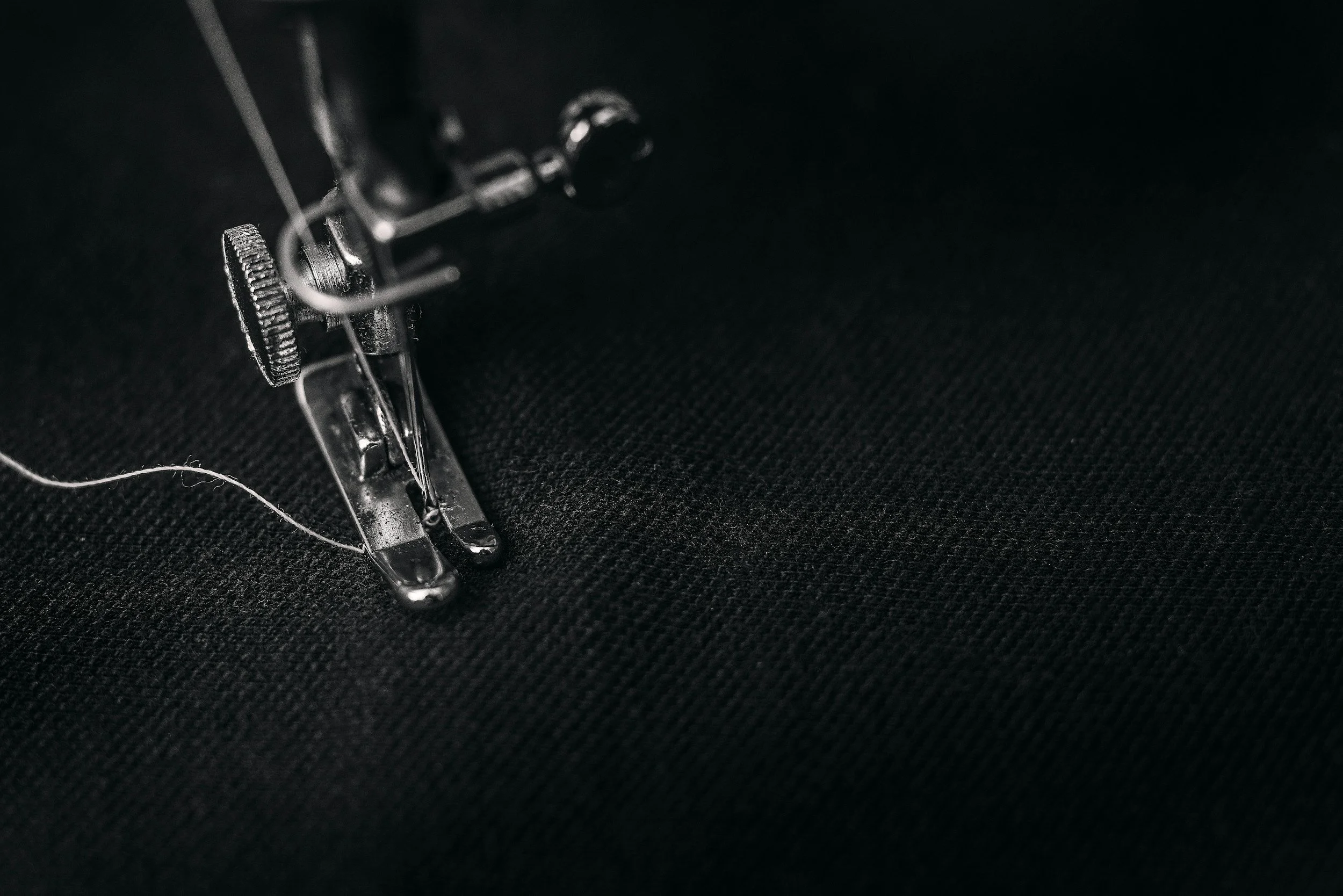Close-up of a sewing machine needle and presser foot on black fabric.