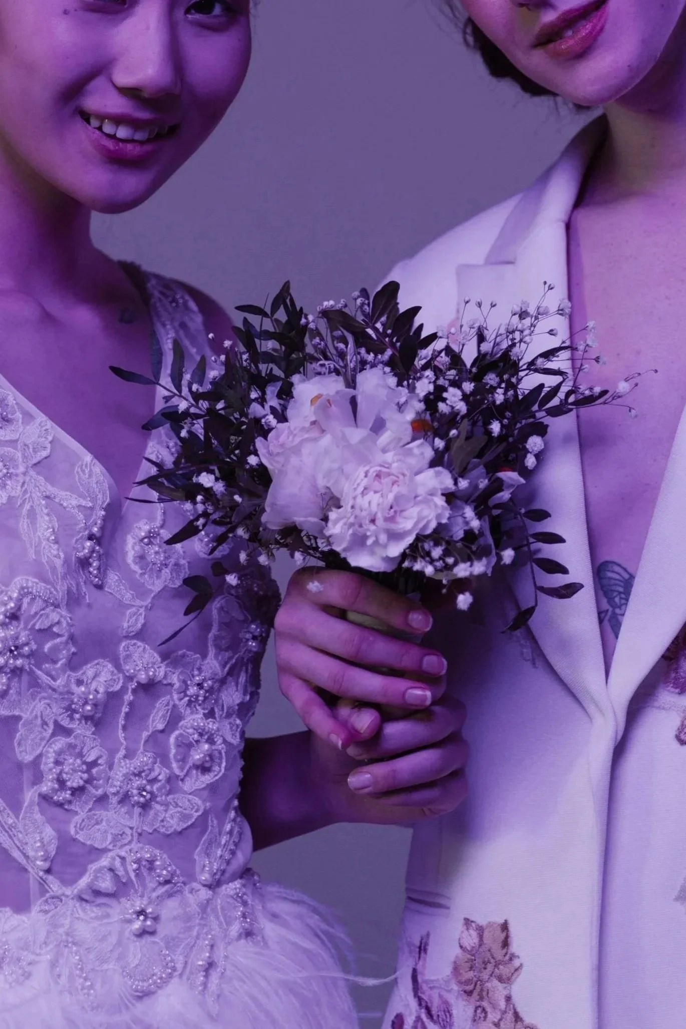 Two women holding a bouquet of white flowers, smiling, with purple lighting effect.