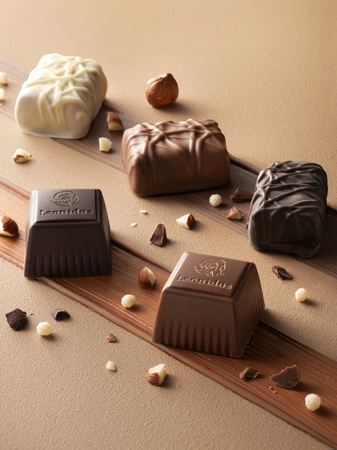 Assorted chocolates, including white, milk, and dark chocolate, with chopped nuts and sprinkled decoration on a beige background.