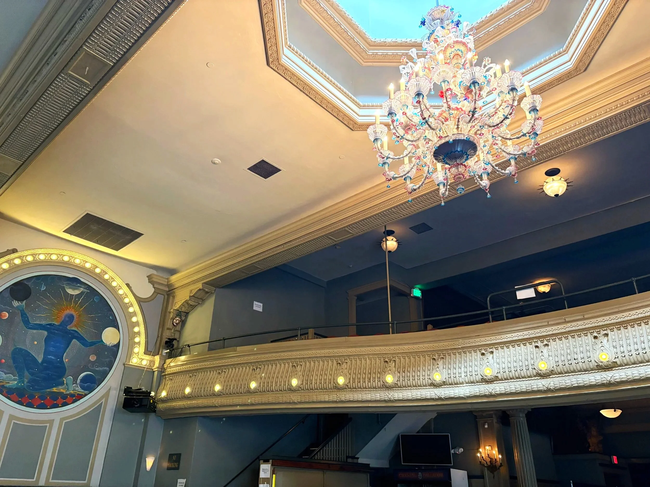 An ornate chandelier hanging from a ceiling with decorative trim in an elegant interior space.