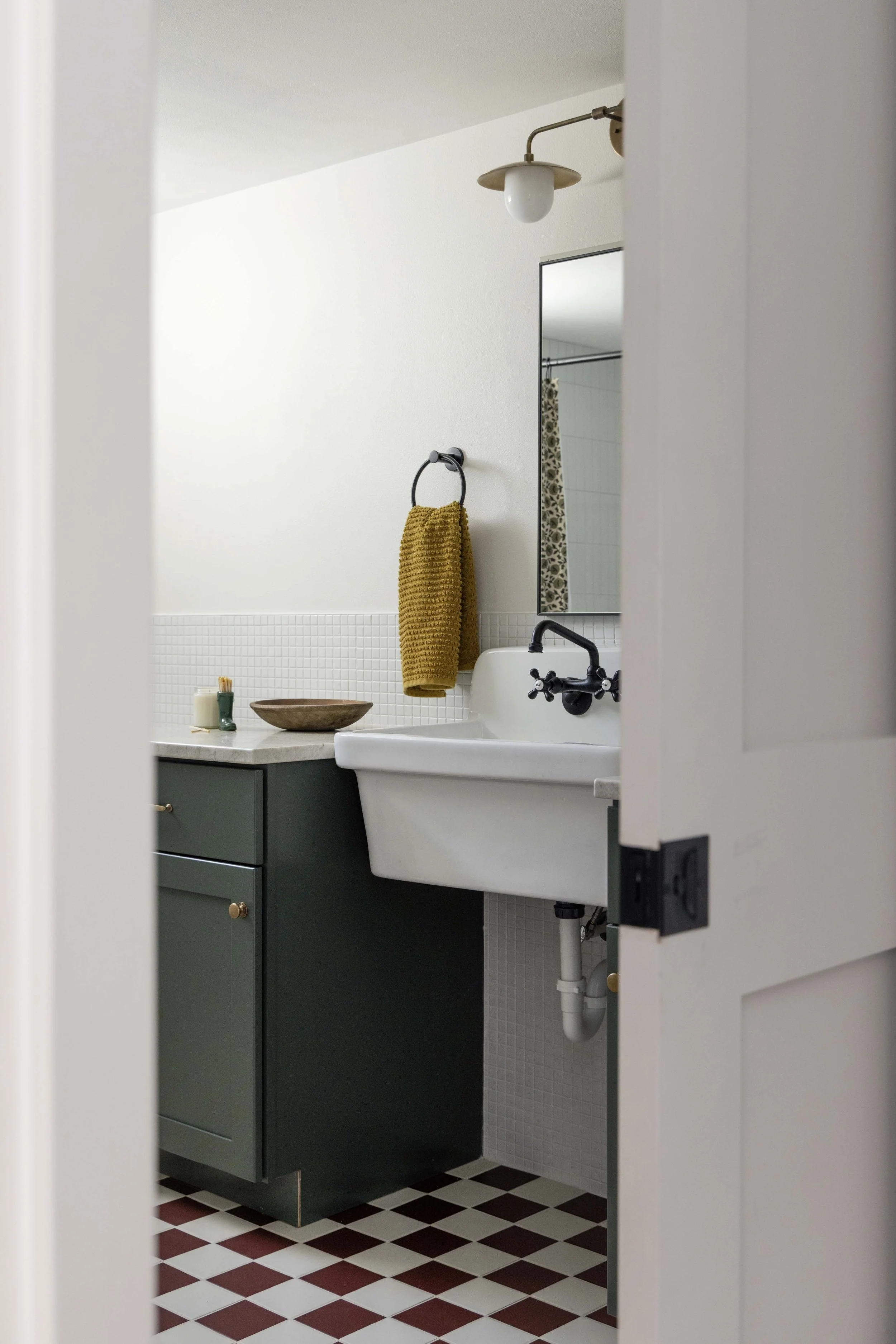 Basement powder room peek featuring a white wall-mount sink with black fixtures by Root Down Remodeling.