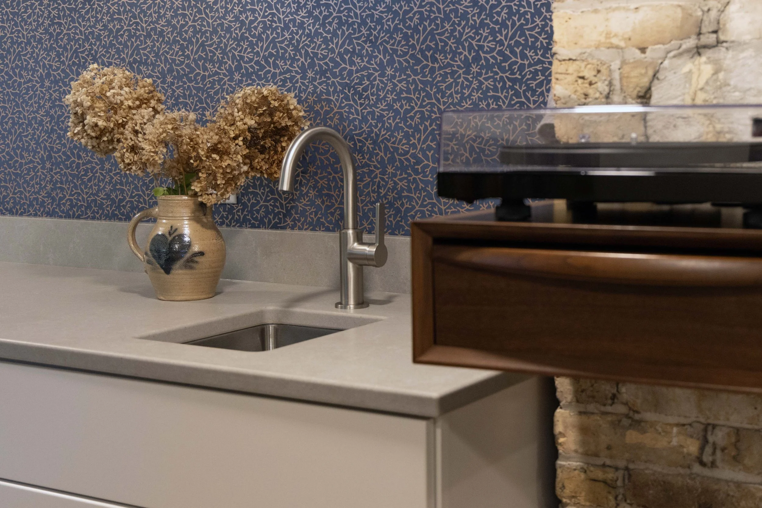 Wet bar area detail showing a stainless steel undermount sink, gooseneck faucet, and a vintage record player station.
