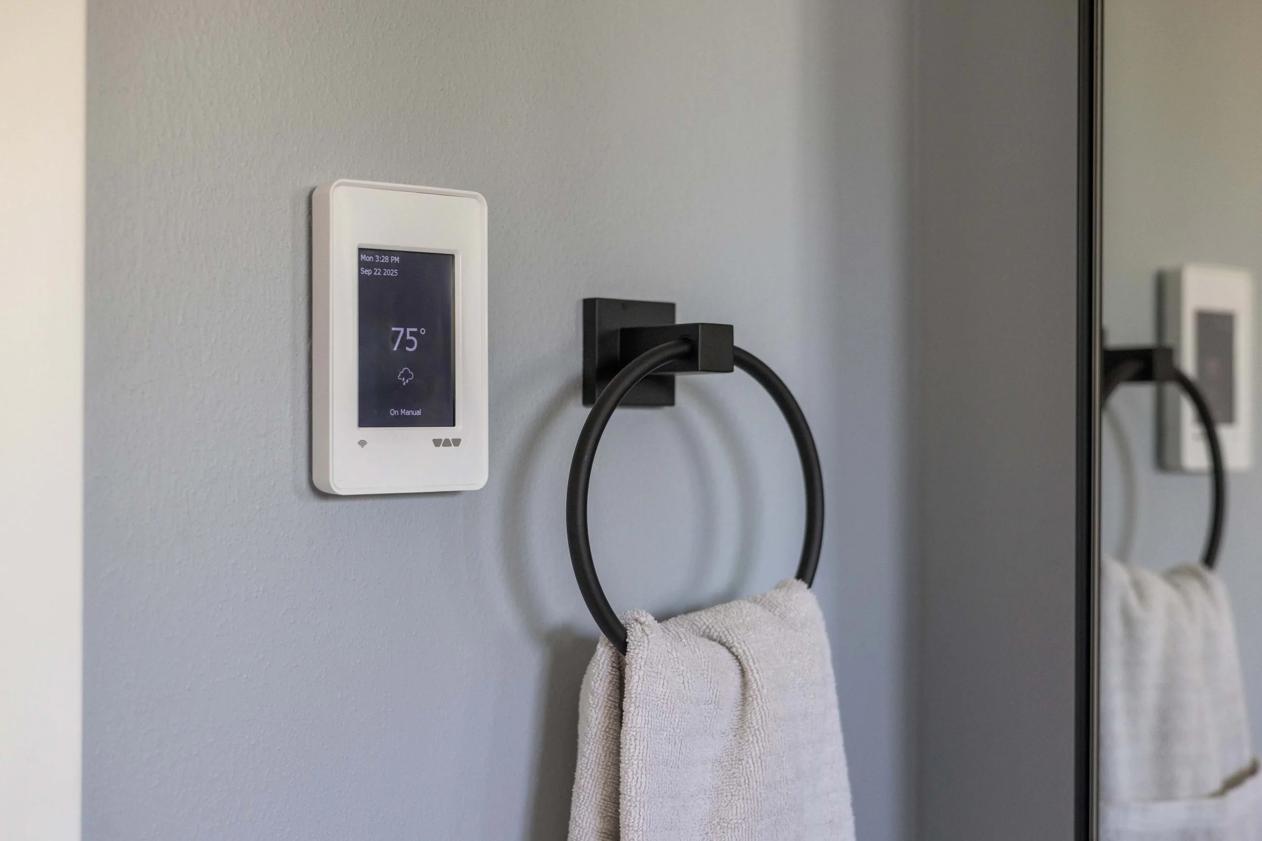 Digital wall thermostat controller mounted next to a matching matte black round towel ring holding a hand towel.