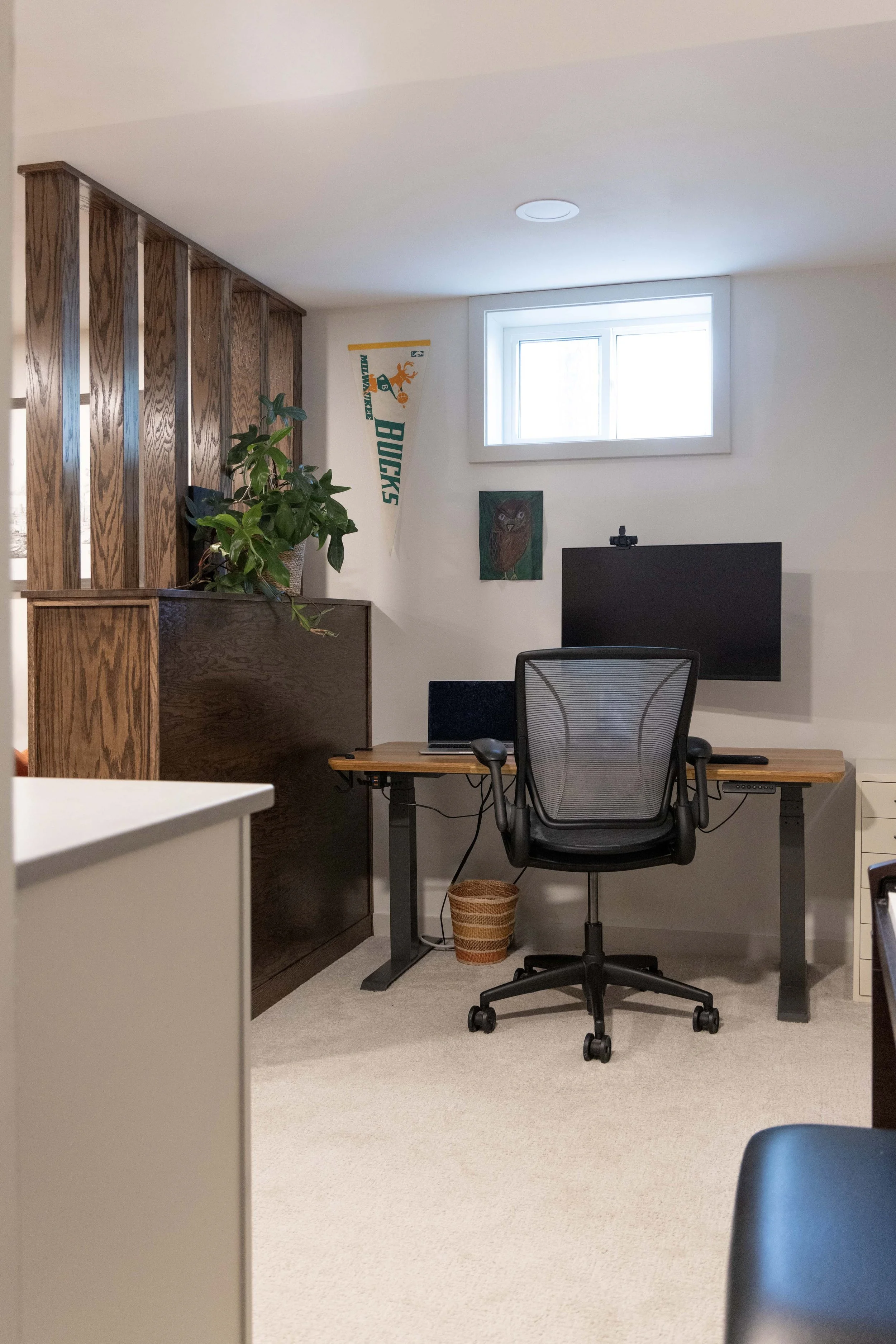 Basement home office nook featuring a wood desk, ergonomic chair, and custom wood divider wall.