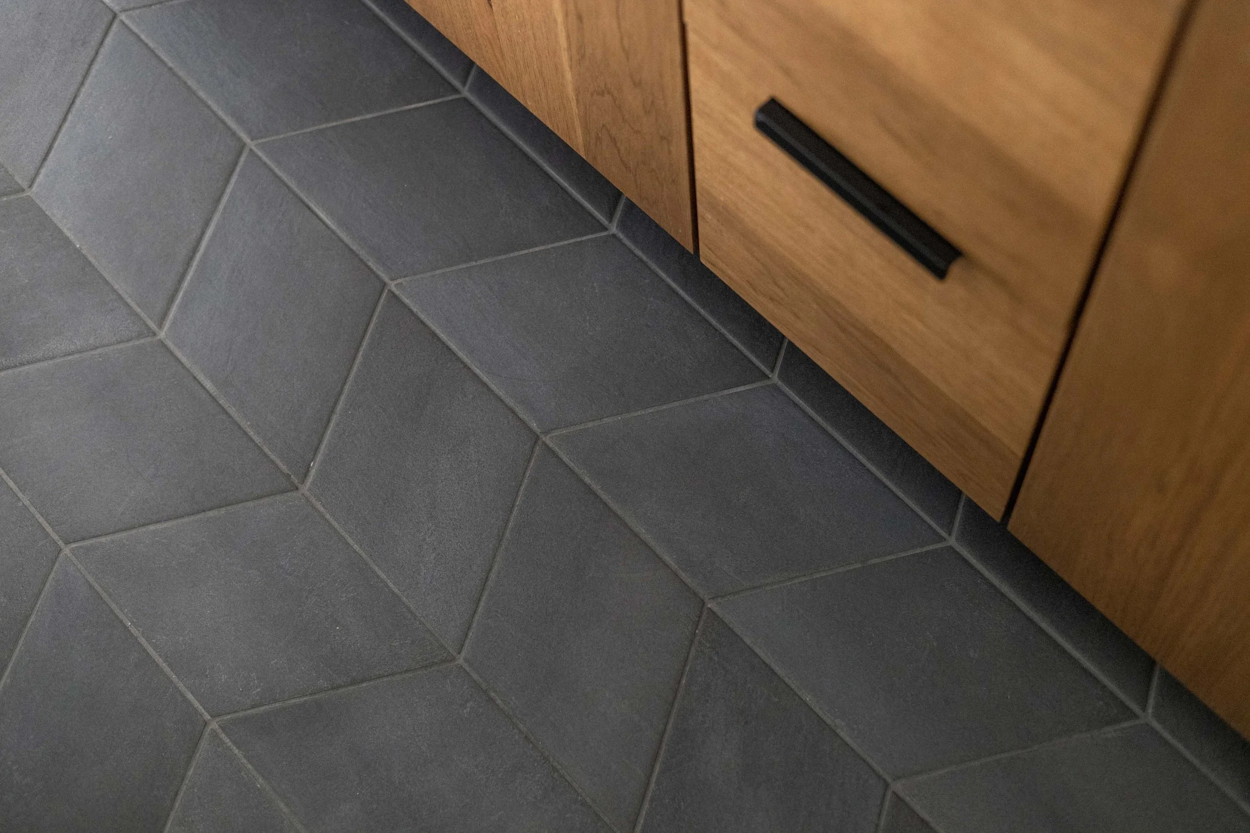 Luxury bathroom flooring showcasing dynamic dark charcoal hexagon floor tiles meeting custom oak vanity cabinets.