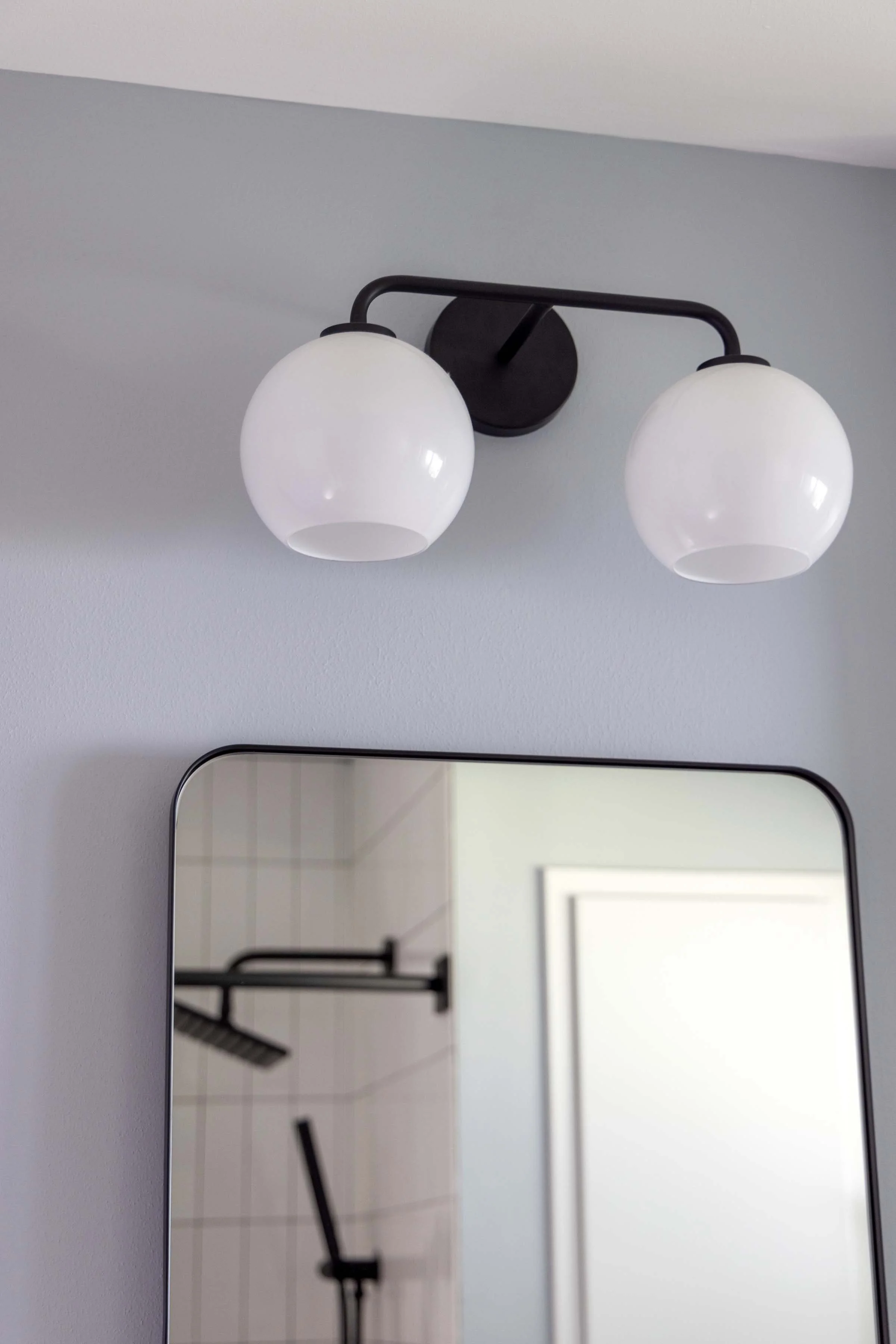 Modern black double-globe vanity light fixture mounted over a thin black-framed bathroom mirror.