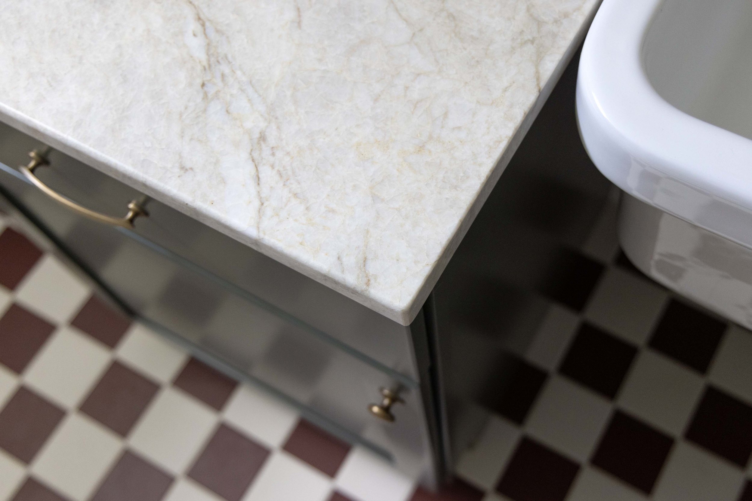 Detail shot of a veined quartz vanity countertop, dark cabinets, and a classic checkered floor tile pattern.