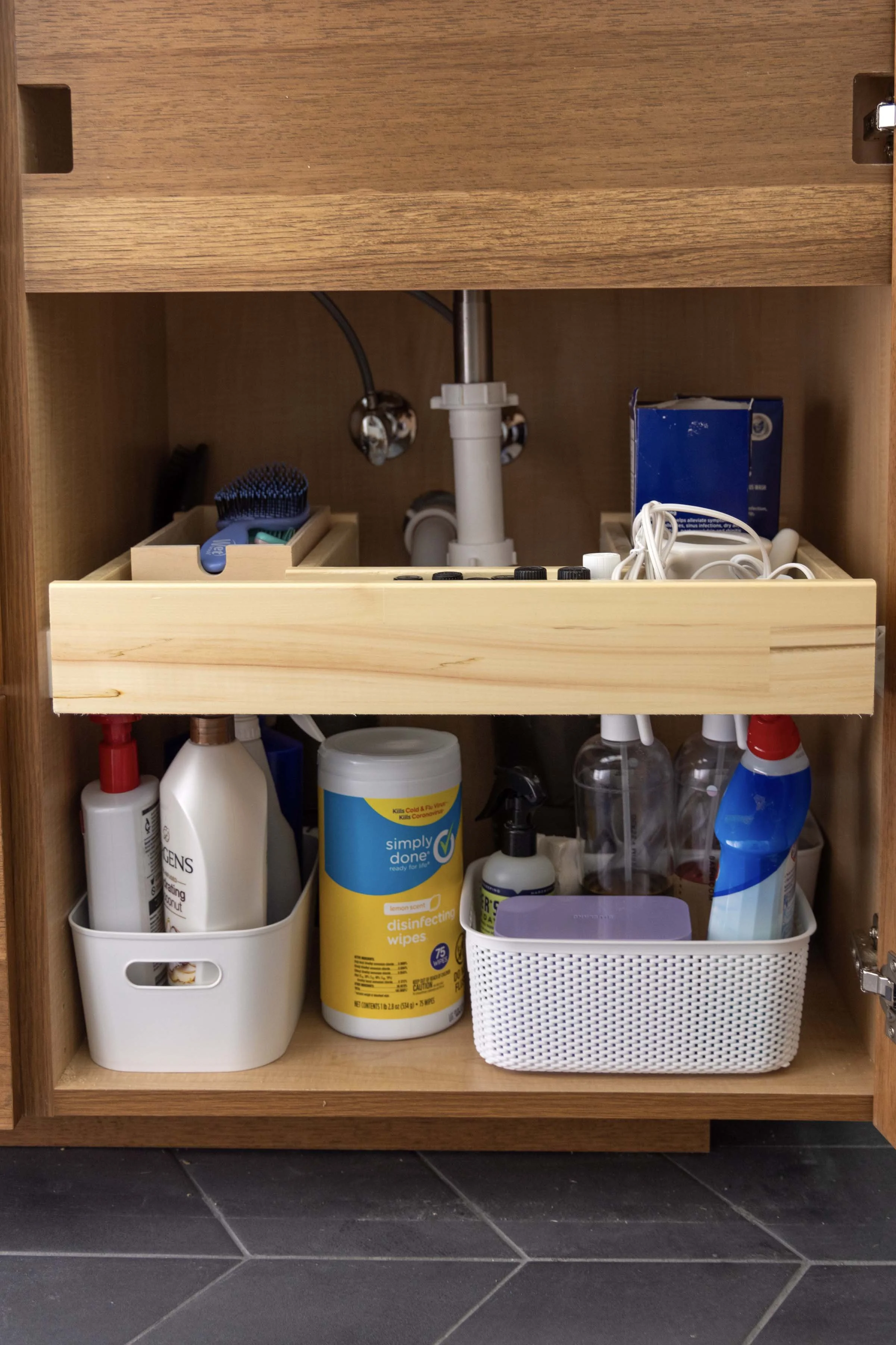 Functional bathroom organization showing a wooden under-sink slide-out shelf fitted around drain pipes.