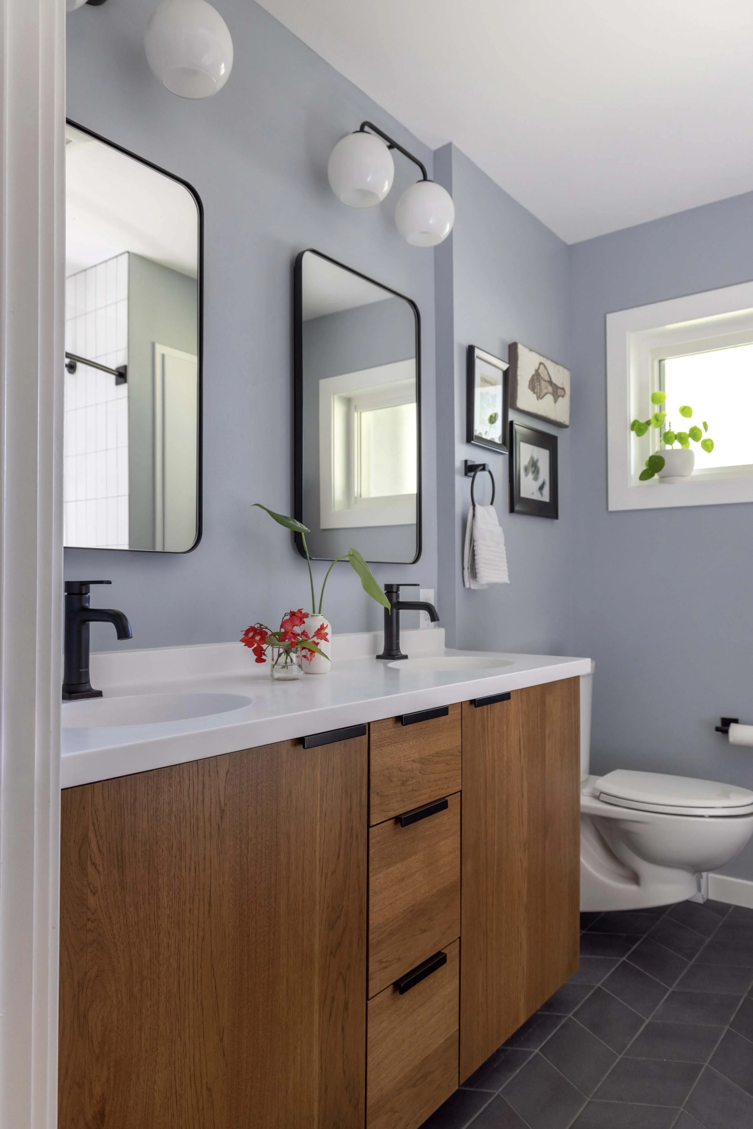Primary bathroom renovation by Root Down Remodeling showing light blue walls, a wood vanity, and toilet alcove.