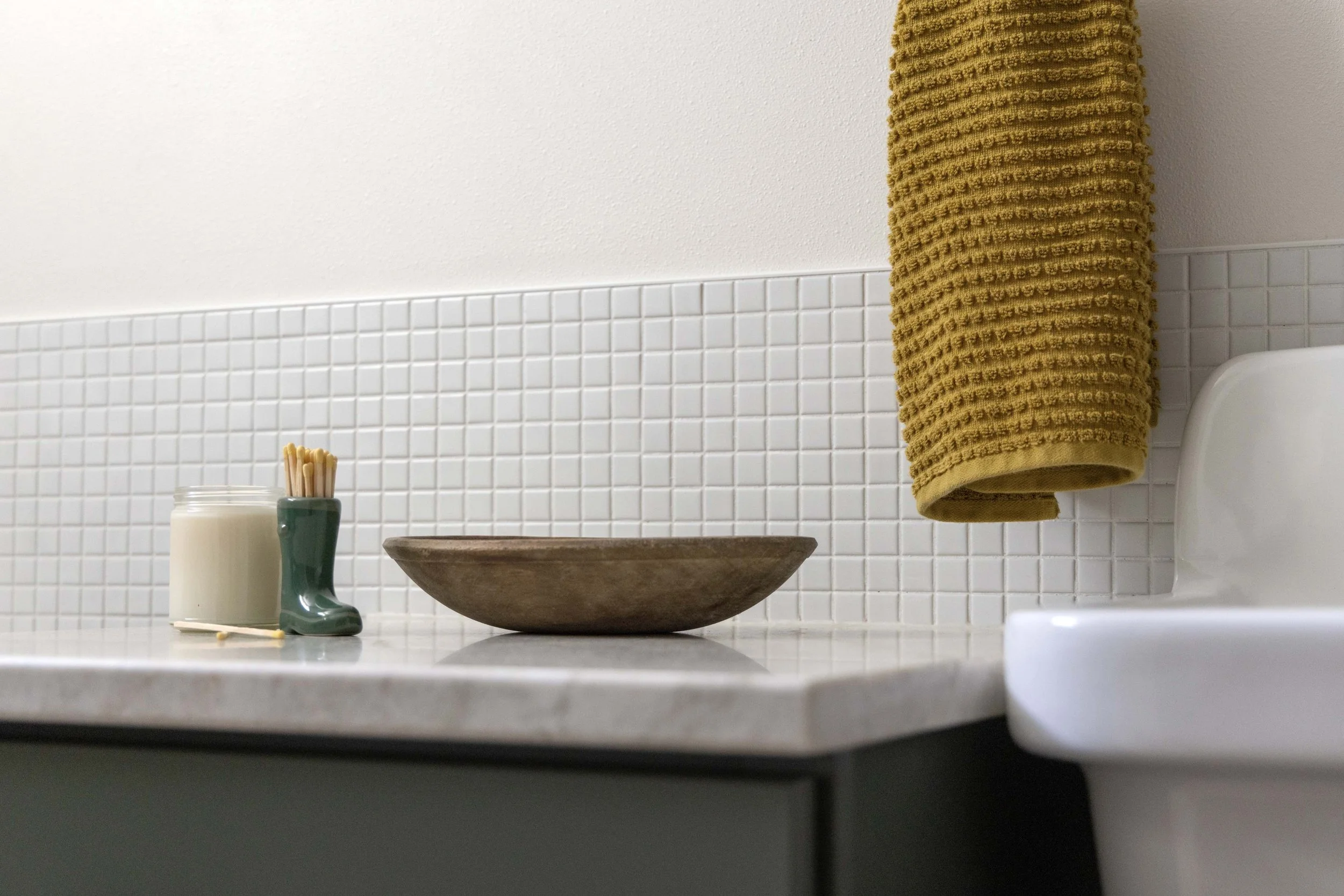Close-up detail of white square mosaic wall tile, quartz countertops, and a green bathroom vanity cabinet.
