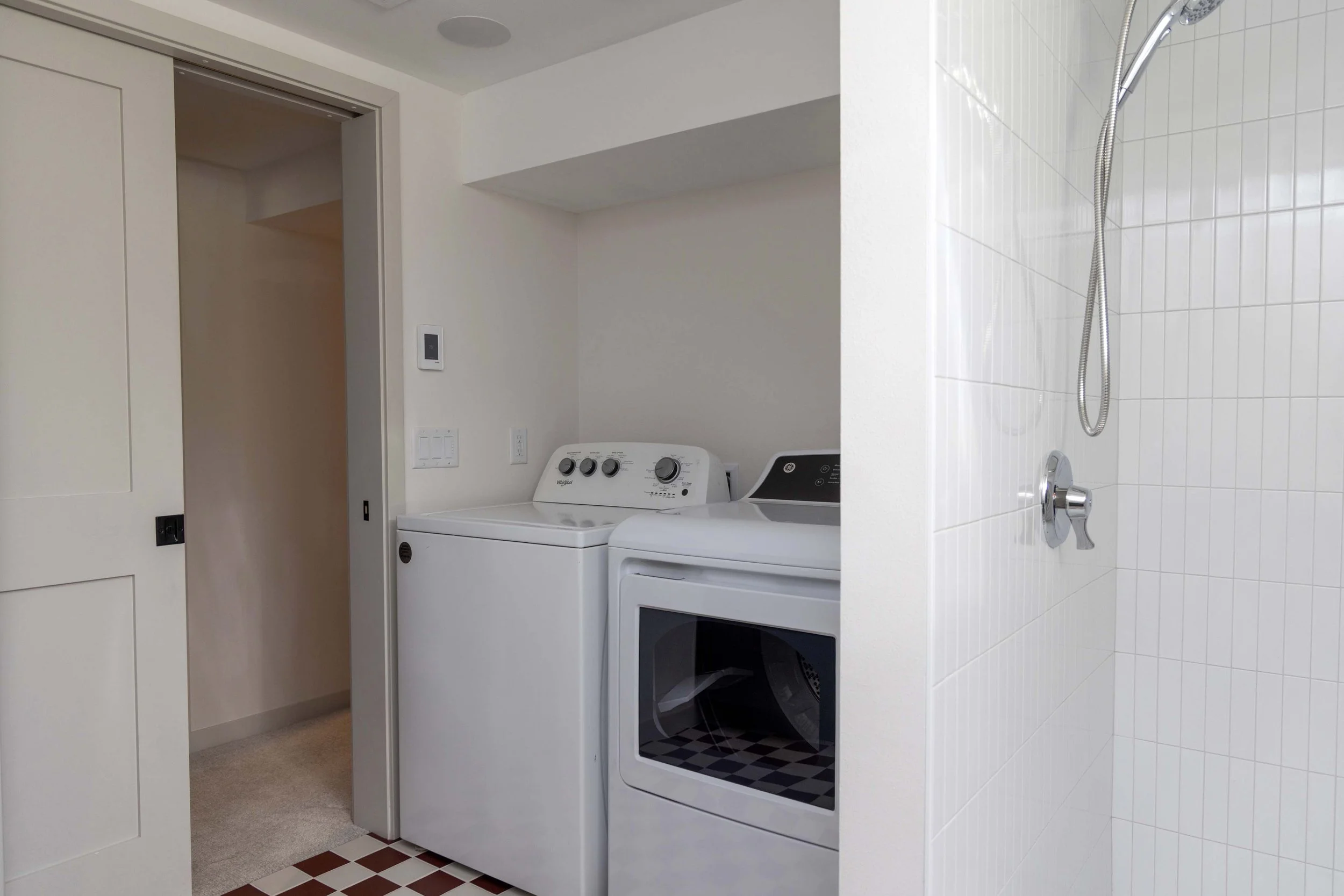 Compact basement laundry room alcove featuring a white washer, dryer, and adjacent tile shower stall.