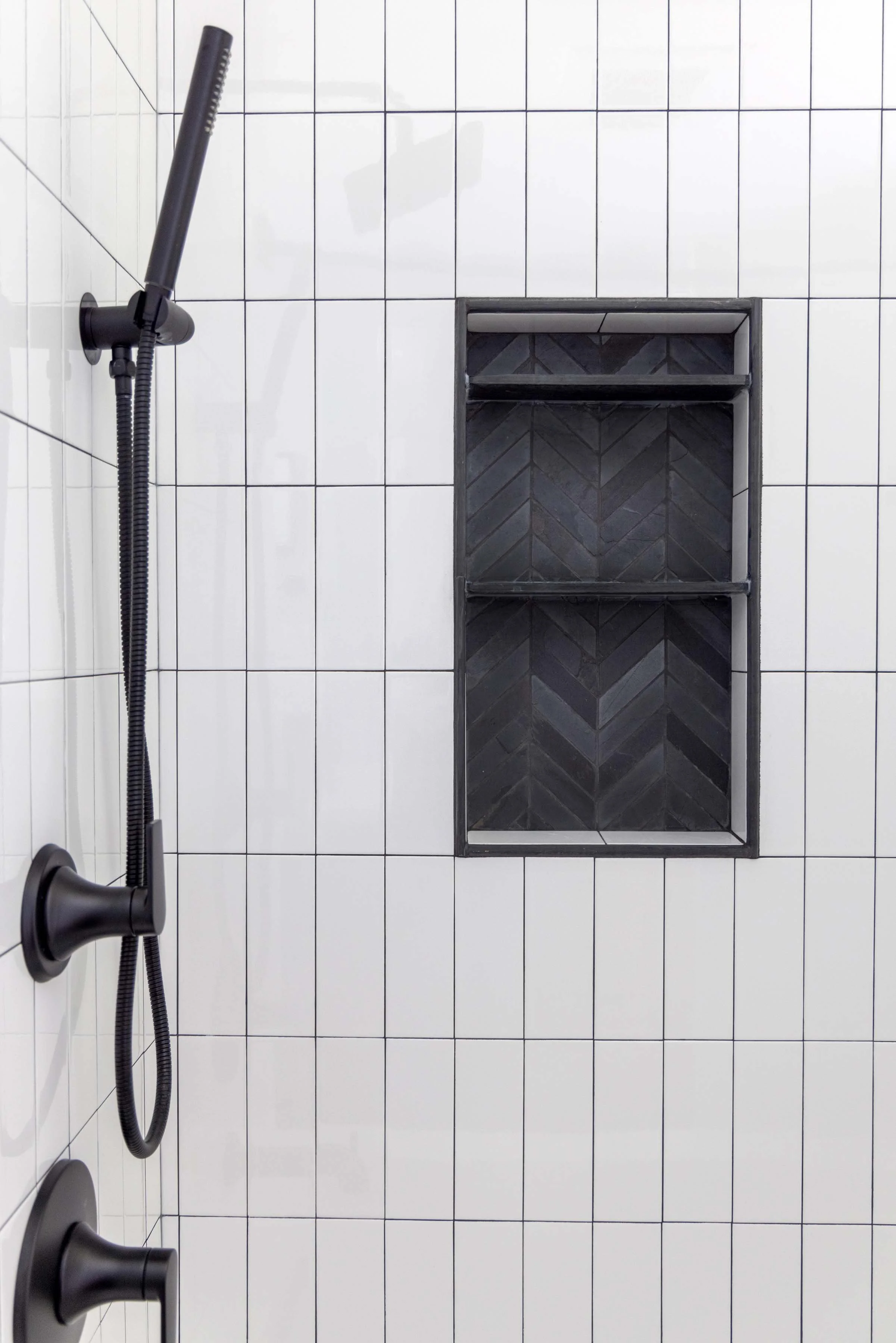 Vertical stack white shower tile installation showcasing a recessed storage niche with dark chevron accent tiles.