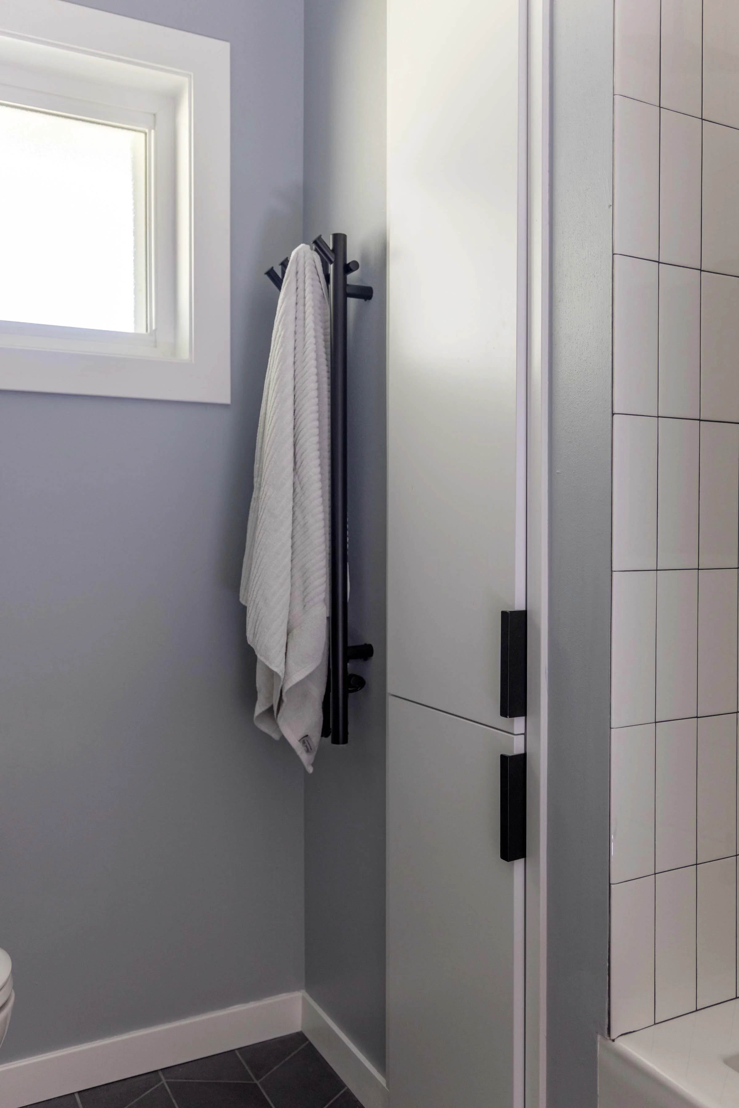 Modern primary bathroom accent wall featuring a minimalist wall-mounted matte black vertical towel warmer rack.