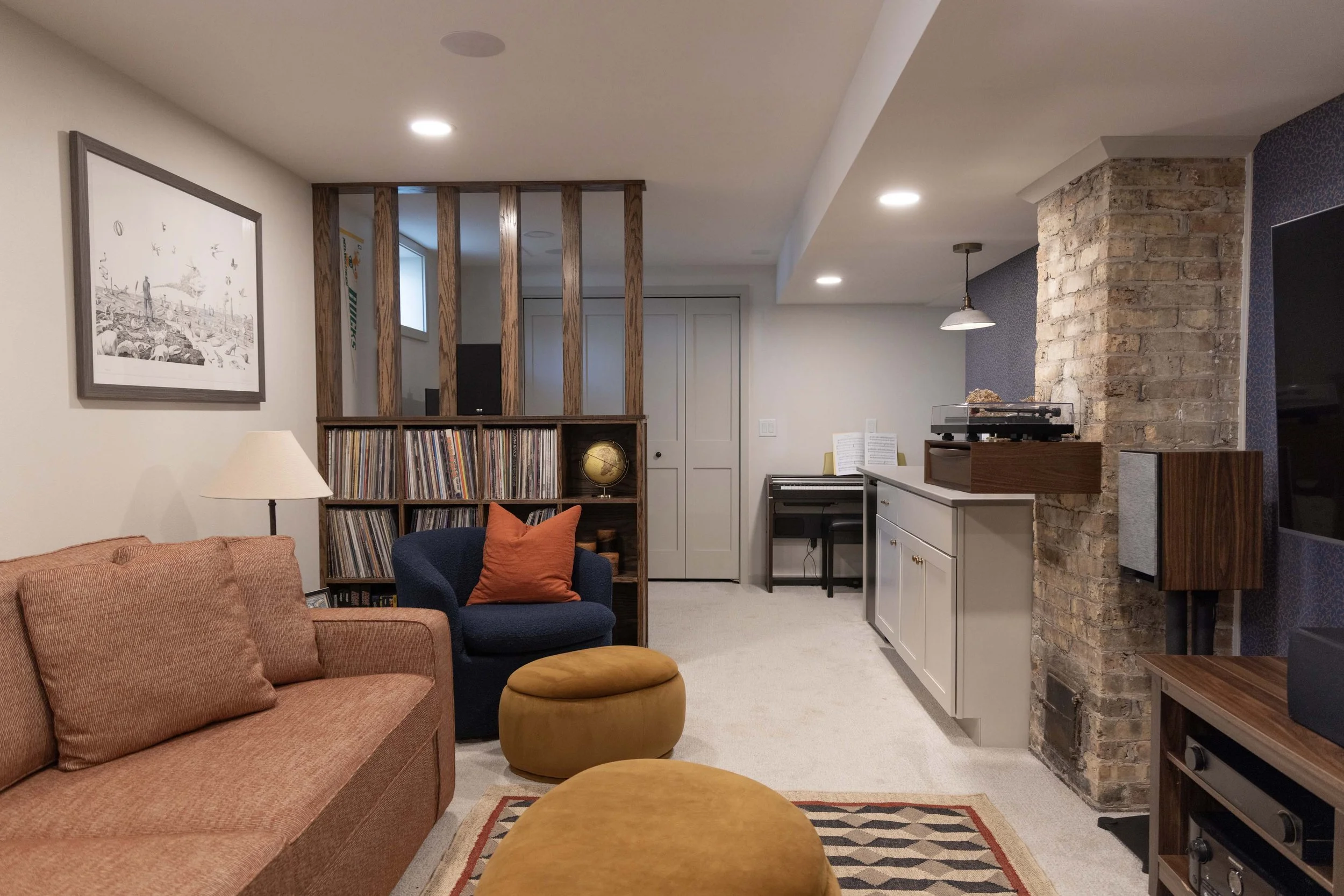 Living room with a peach-colored sofa, a navy armchair with an orange pillow, a bookshelf with records and a globe, a brick wall, and a white cabinet with a turntable on top.