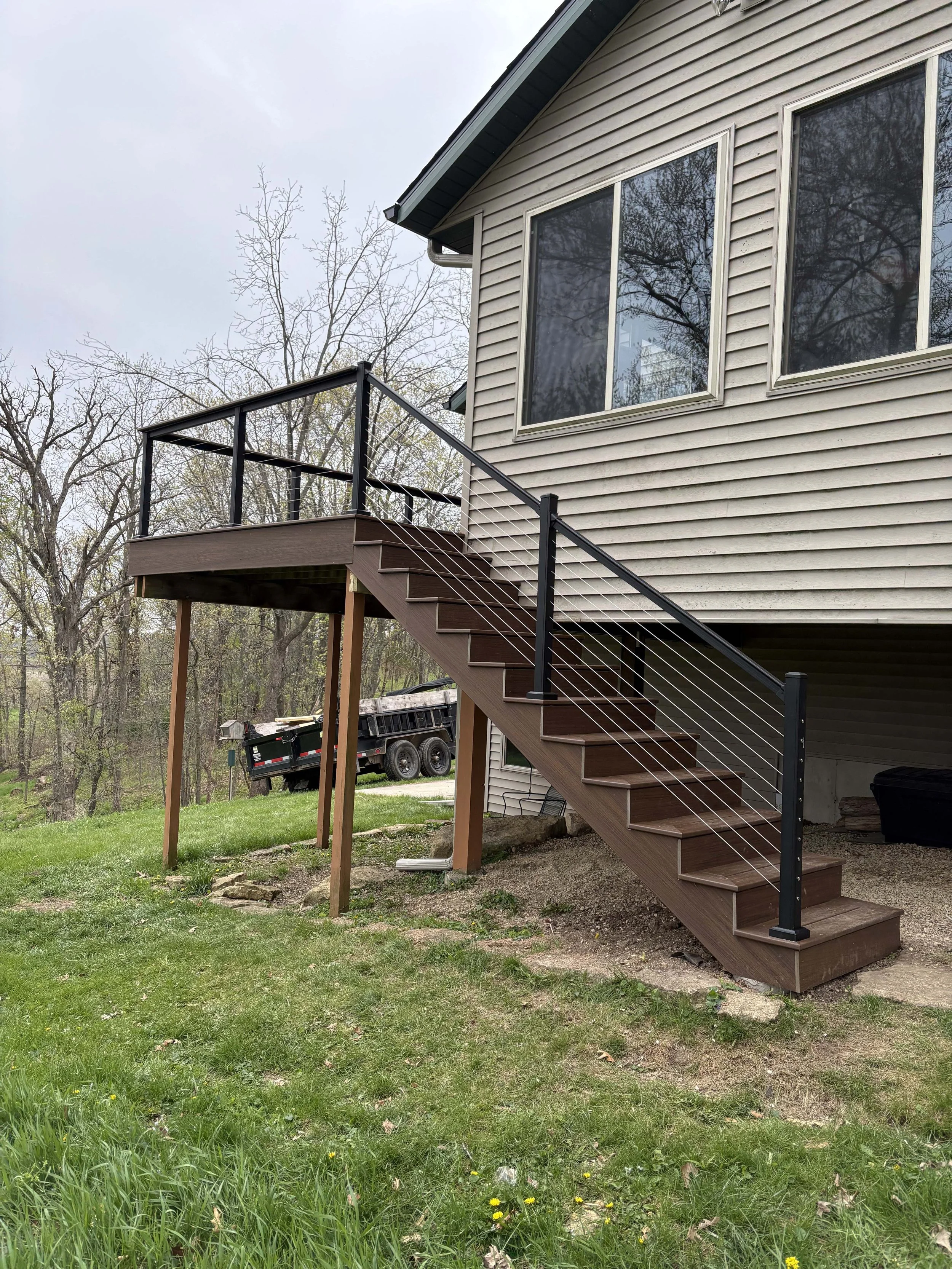 Elevated composite deck built by Root Down Remodeling featuring an attached staircase and black aluminum balusters.