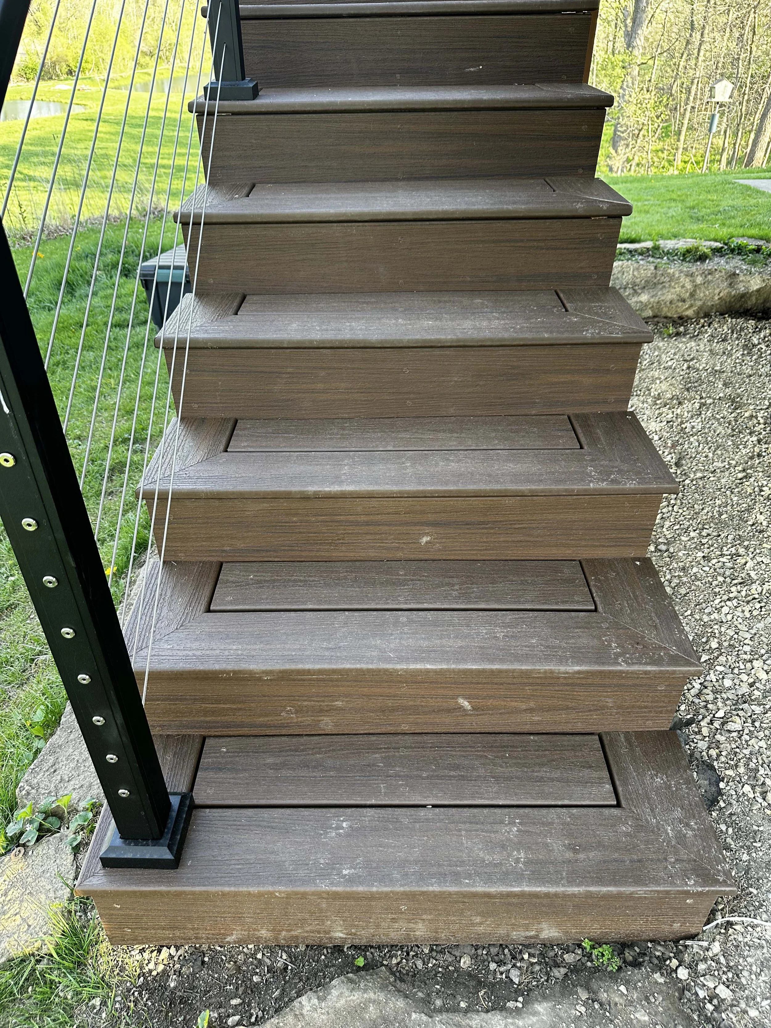 Close-up detail of outdoor composite stair treads bordered by a modern black metal handrail system.