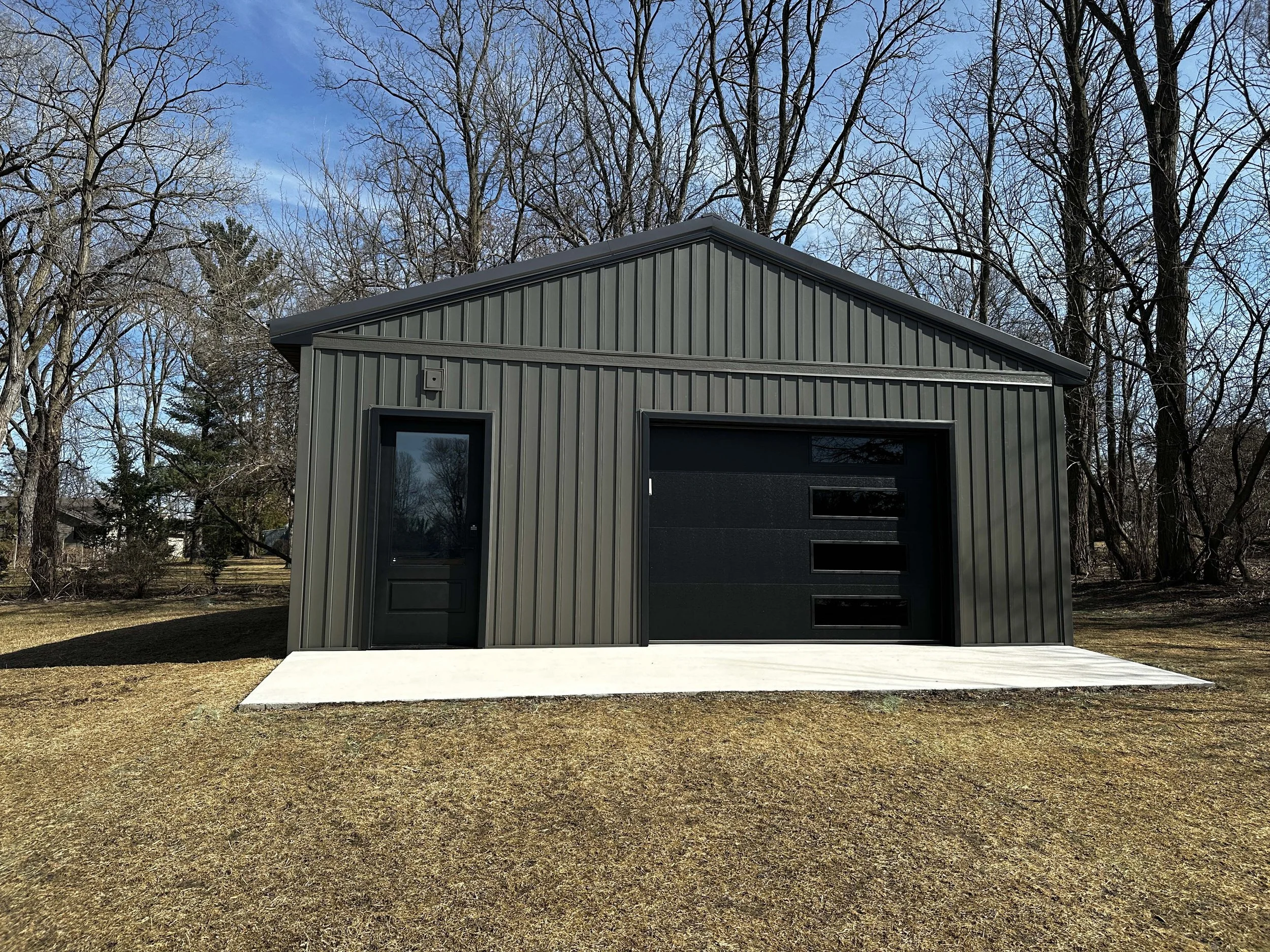 Front view of the metal outbuilding featuring a matching dark entry door.