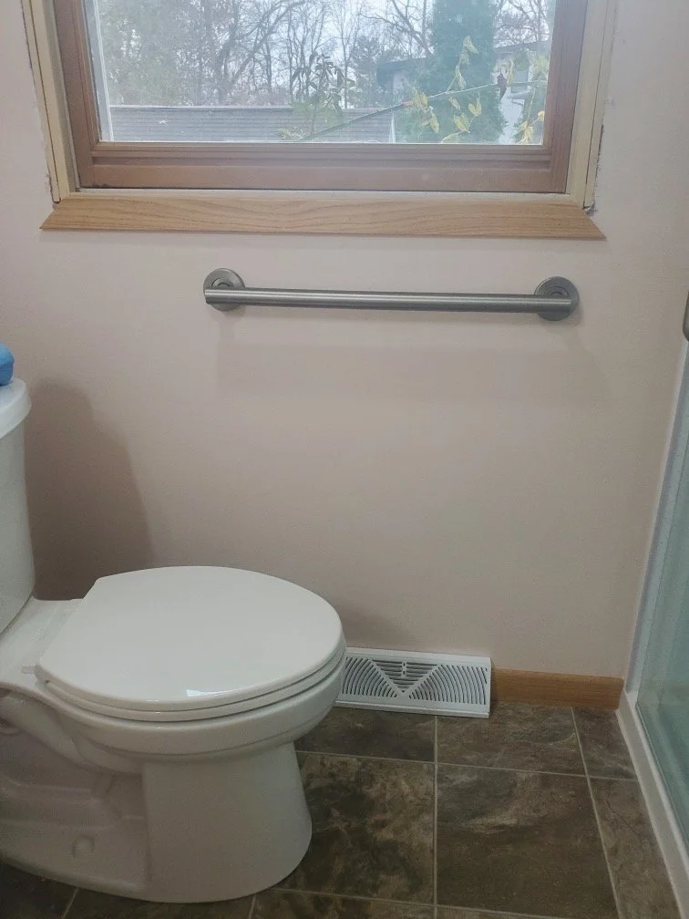 Updated toilet alcove featuring a wall-mounted safety grab bar and wood-framed window.