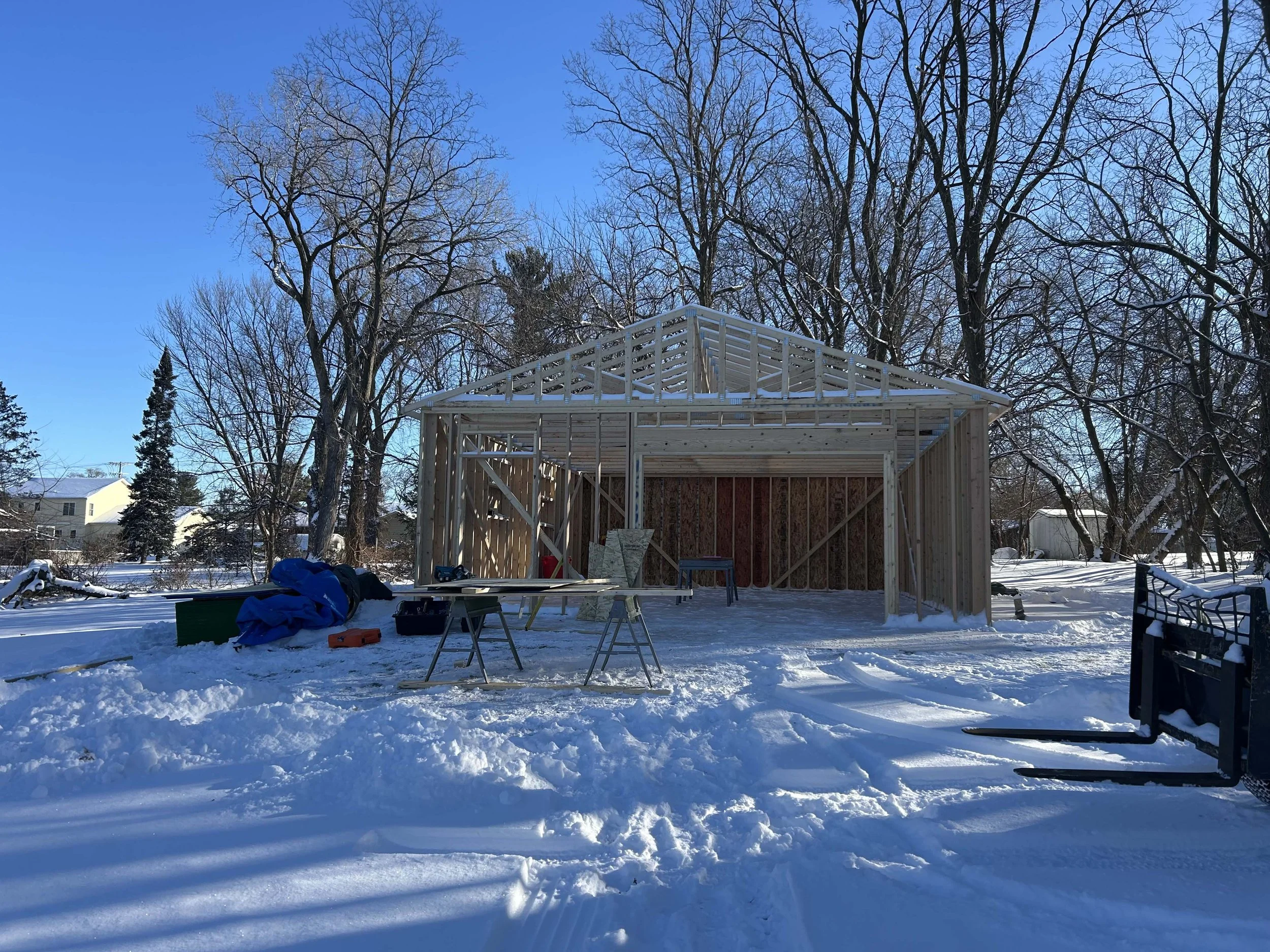 Mid-construction winter phase of a detached garage showing open wood framing.