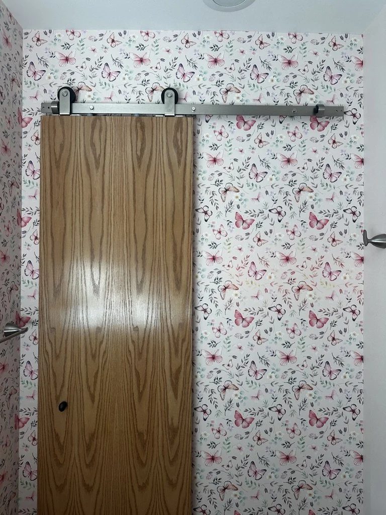 Sliding wood barn door installed against patterned wallpaper.