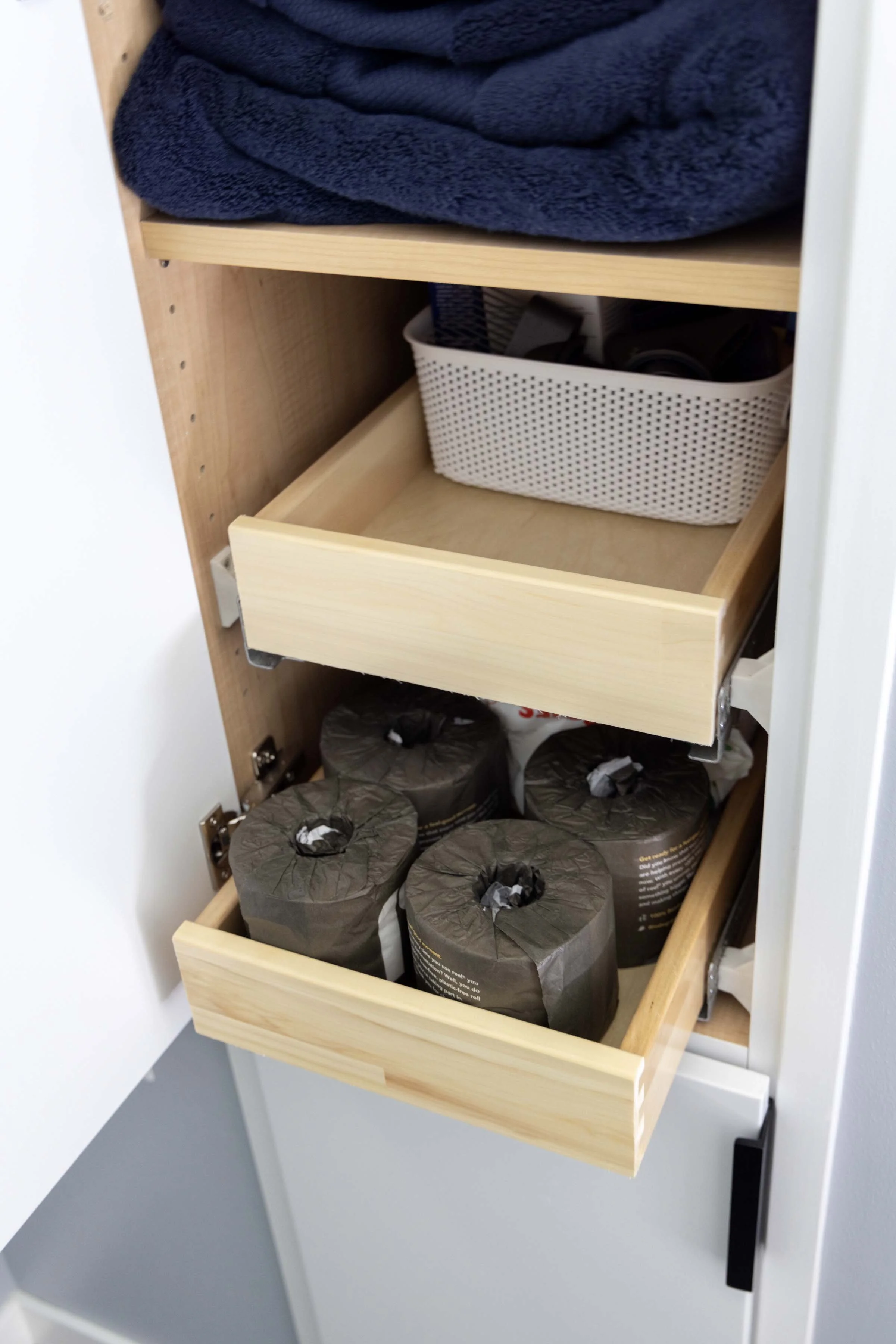Tall bathroom linen cabinet installation featuring built-in wooden pull-out shelves designed for organized toilet paper storage.