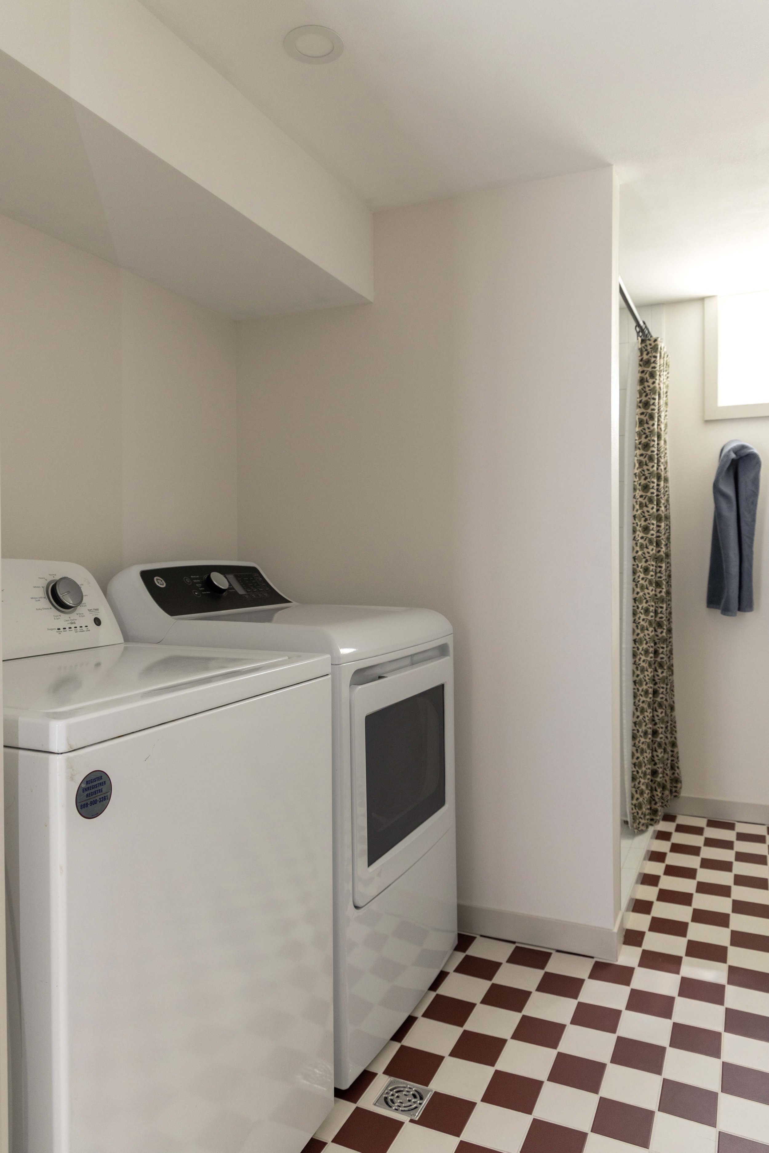 Bright basement laundry alcove with a white washer and dryer unit next to a shower entrance.