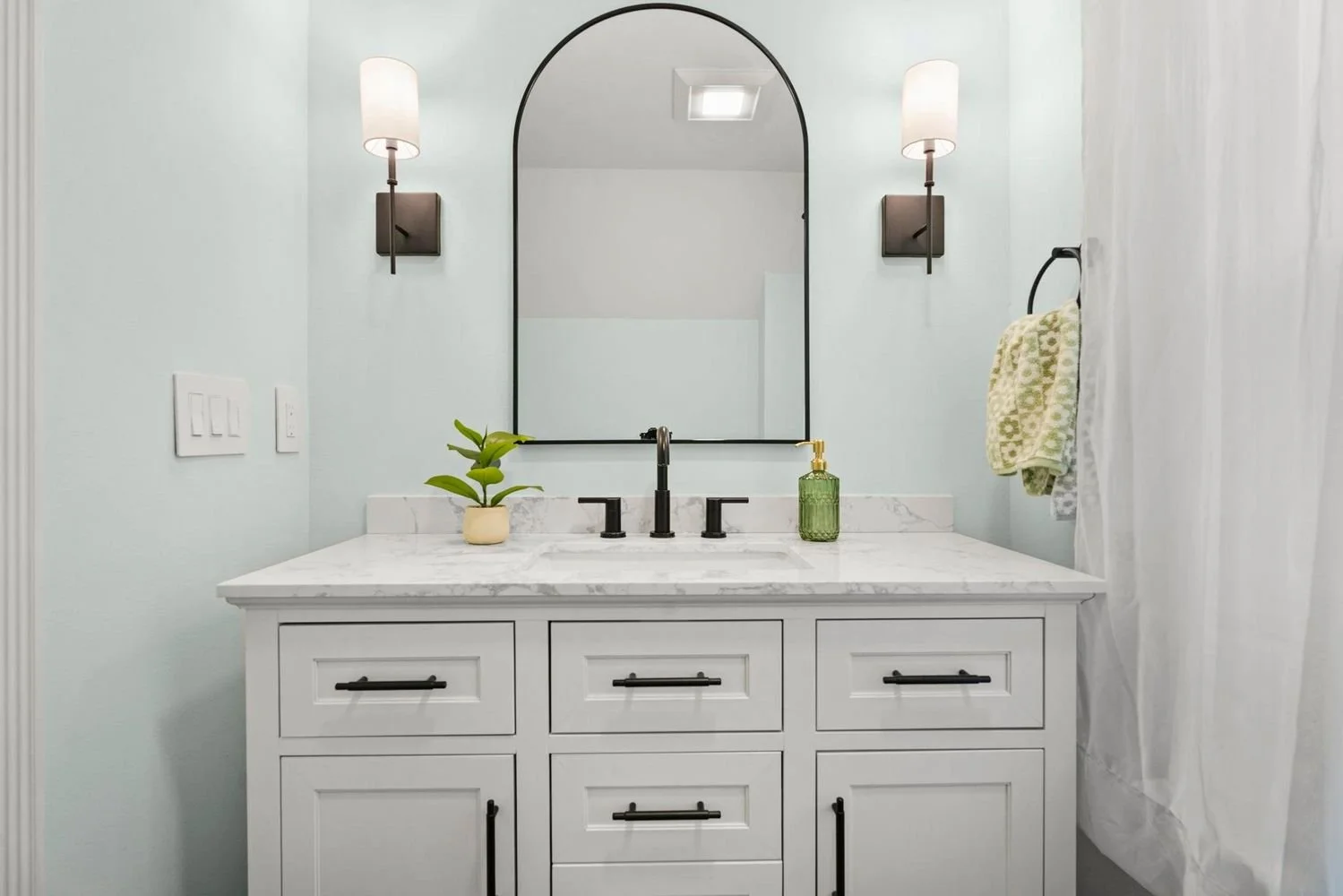 Completed bathroom renovation showcasing a white vanity, an arched black mirror, and modern sconces.