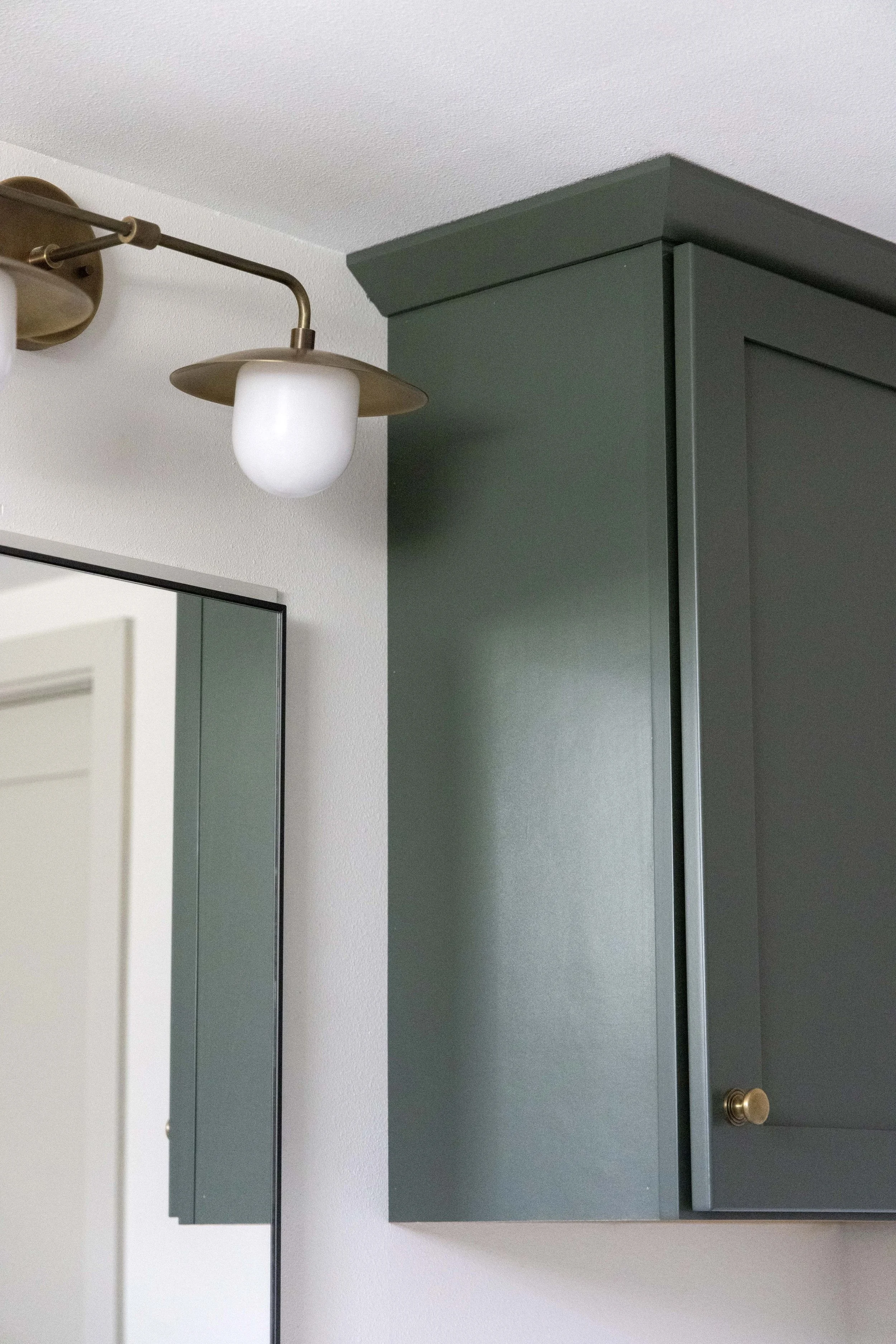 Close-up of a modern brass wall sconce light fixture installed next to dark green painted cabinetry.
