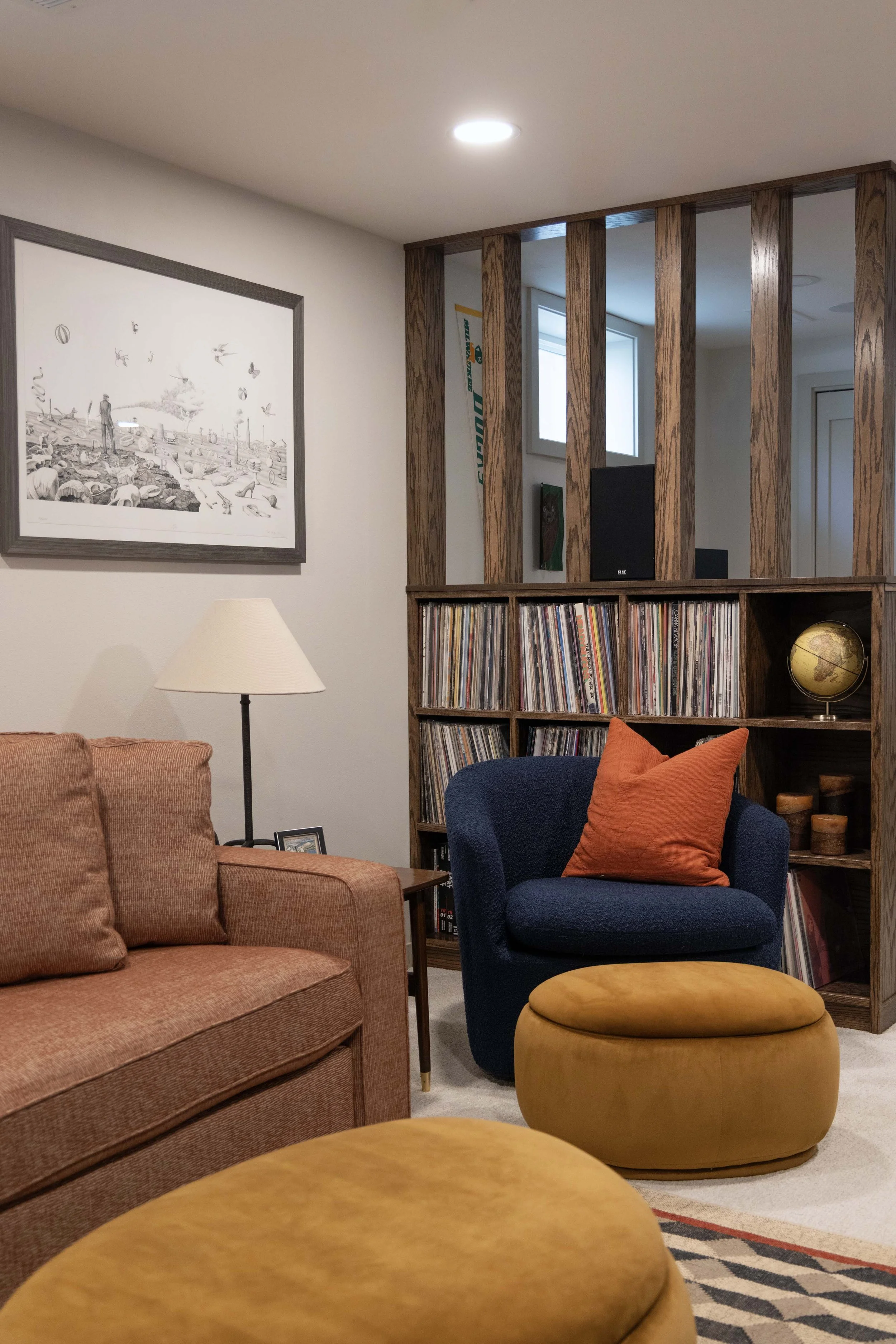 Cozy basement lounge seating area displaying a wood slatted partition shelf filled with records.