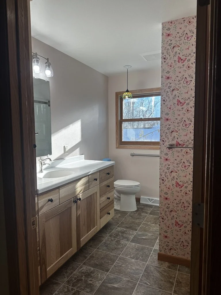 Bright bathroom renovation by Root Down Remodeling with custom wood cabinetry.