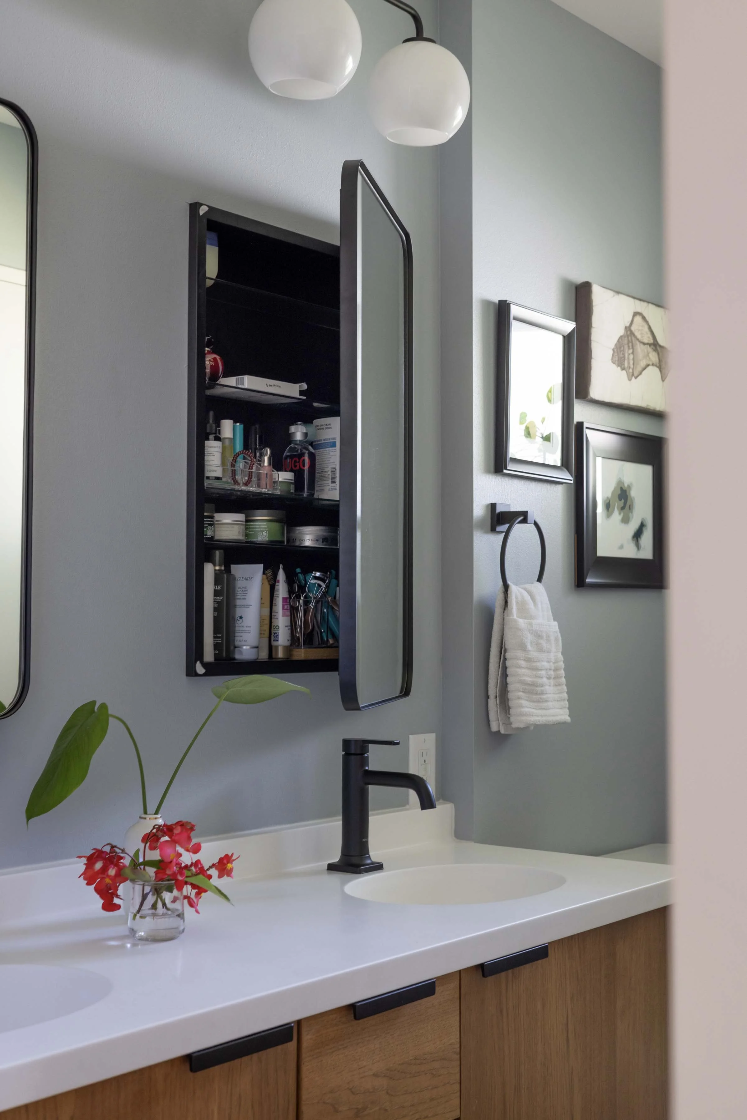 Open surface-mounted black medicine cabinet displaying neatly organized glass shelves and toiletries.