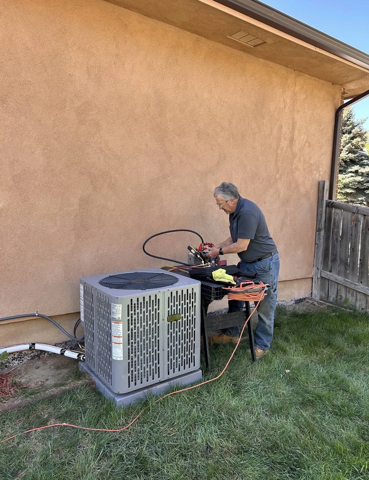 A man working on an air conditioning unit outside a house, using various tools on a work table.