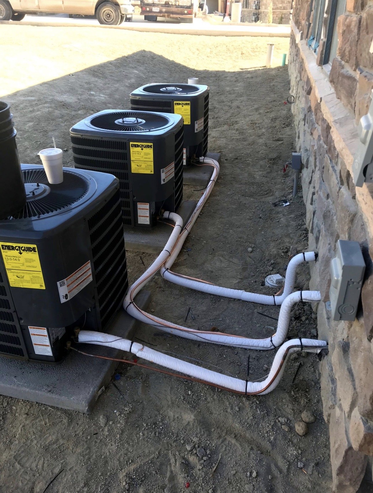 Three HVAC air conditioning units installed outside a building with visible electrical connections and piping.