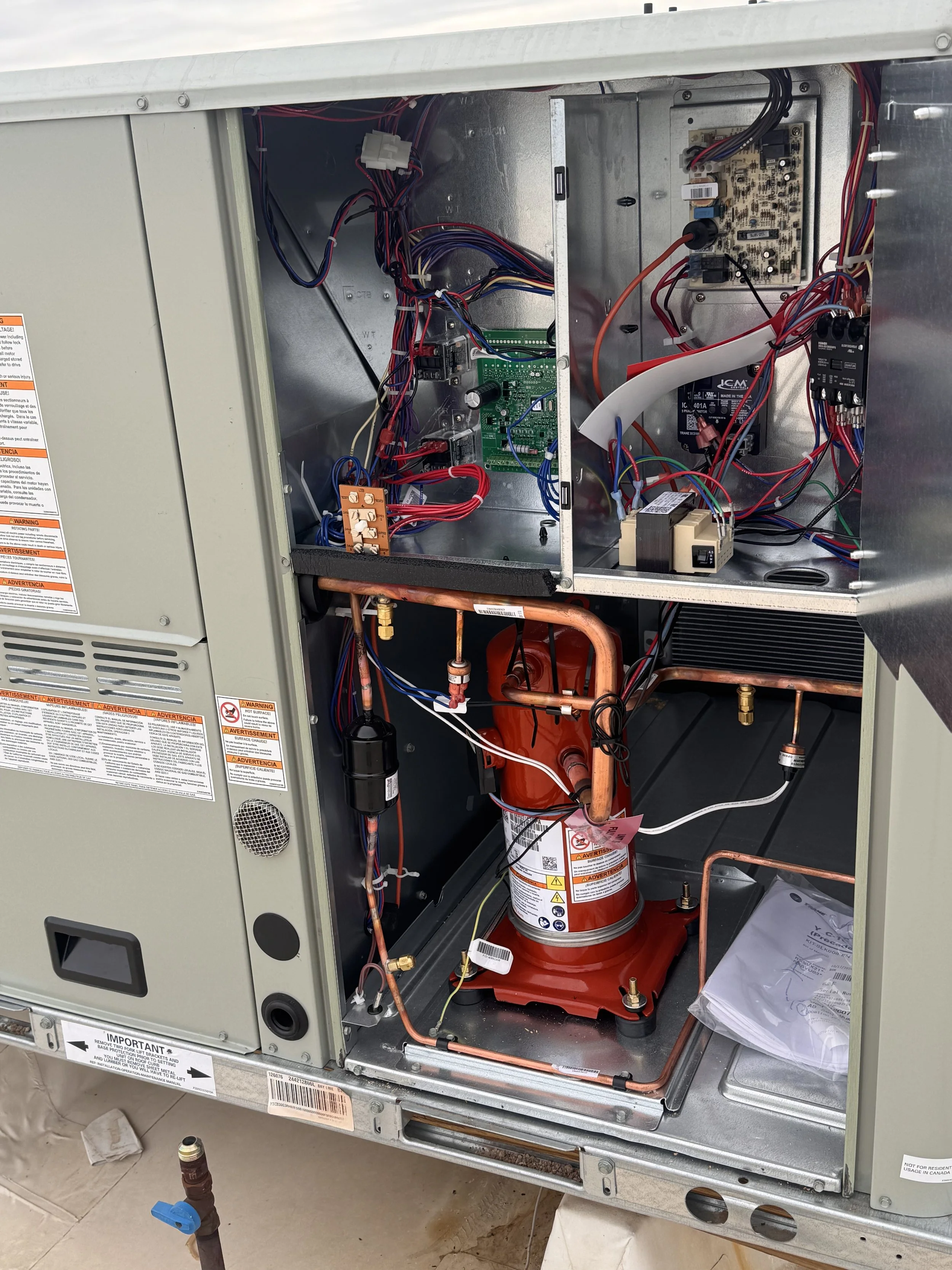 Open HVAC unit revealing internal components including wiring, circuit boards, and a cylindrical fire extinguisher inside the metal casing.