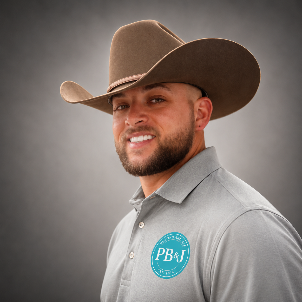 Portrait of a smiling man wearing a cowboy hat and a gray polo shirt with a logo reading 'PB&J Heating and Air Established 2018' against a gray background.